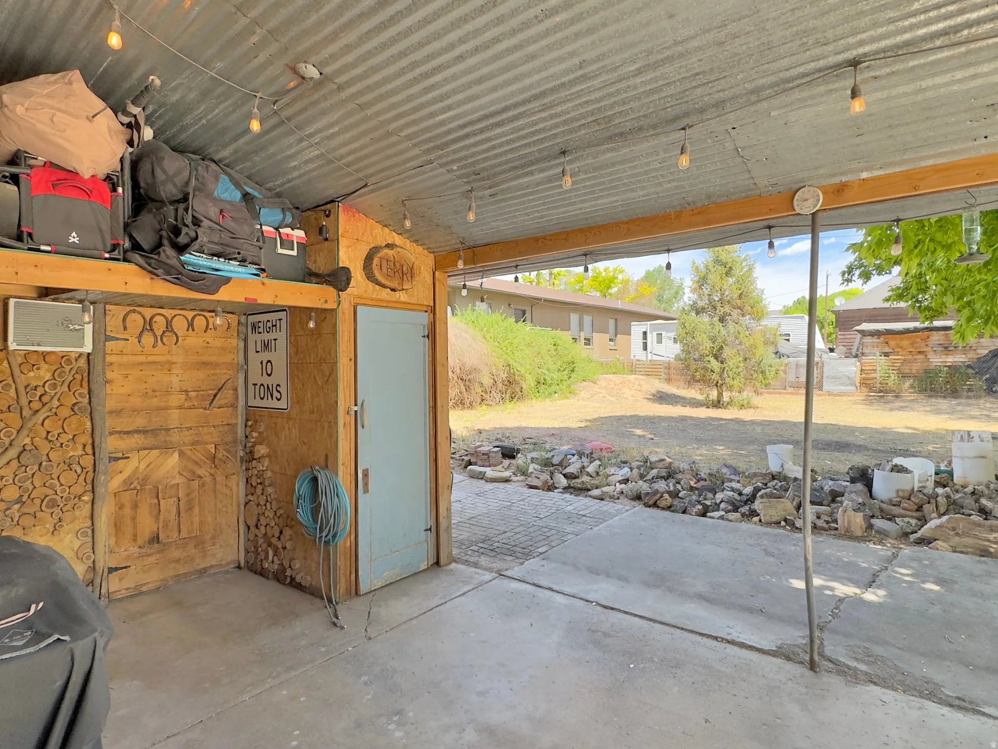 Covered patio with string lighting, corrugated metal roof, wood support beams, and concrete flooring