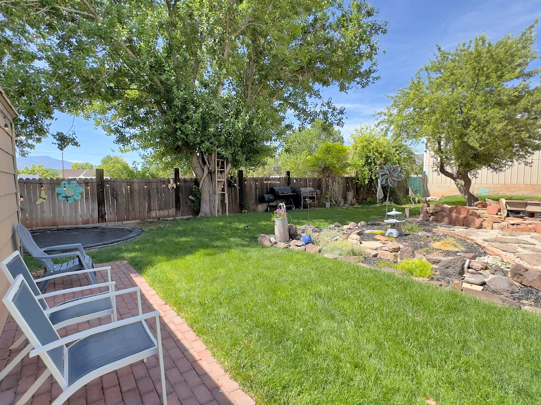 Spacious backyard featuring a manicured lawn, a red brick patio, and mature trees