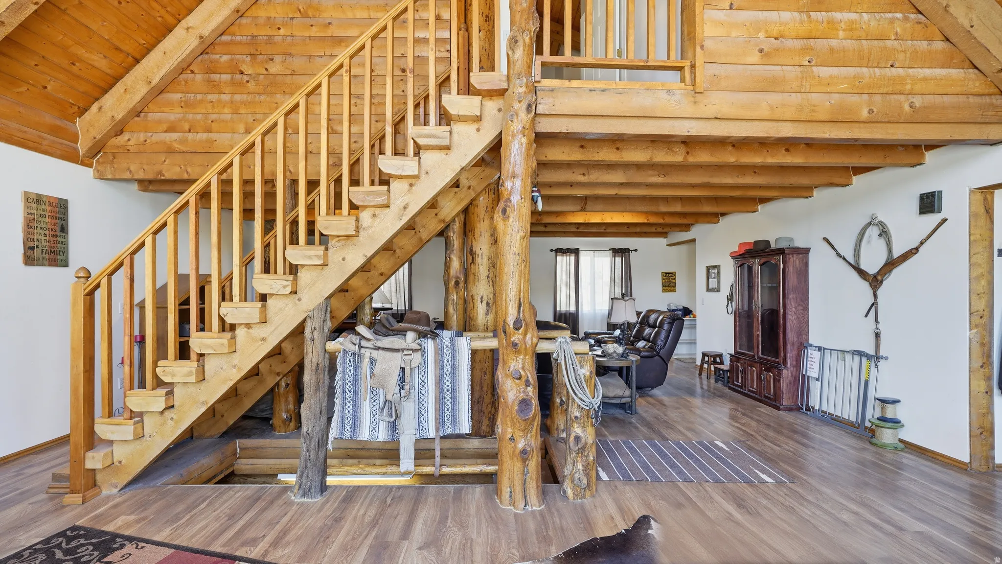 Staircase featuring light wood construction with open risers, log-style support posts, wood-finish flooring, and exposed wood ceiling beams