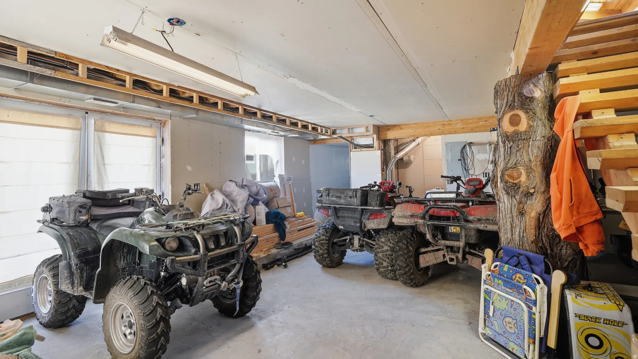 Utility space featuring concrete flooring, exposed wood beams, and a fluorescent light fixture