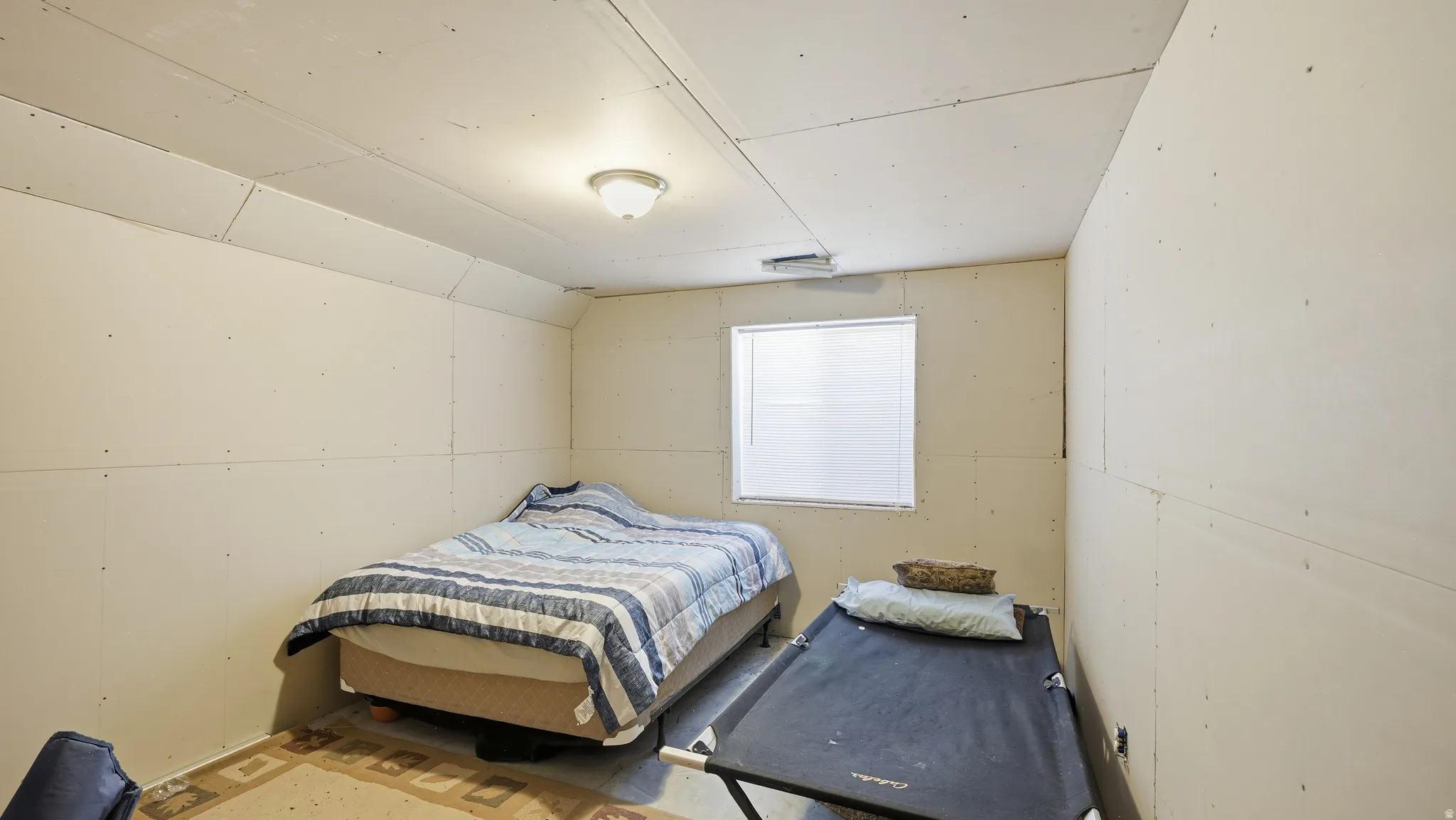 Room featuring a window with horizontal blinds, a ceiling-mounted light fixture, and walls finished with drywall