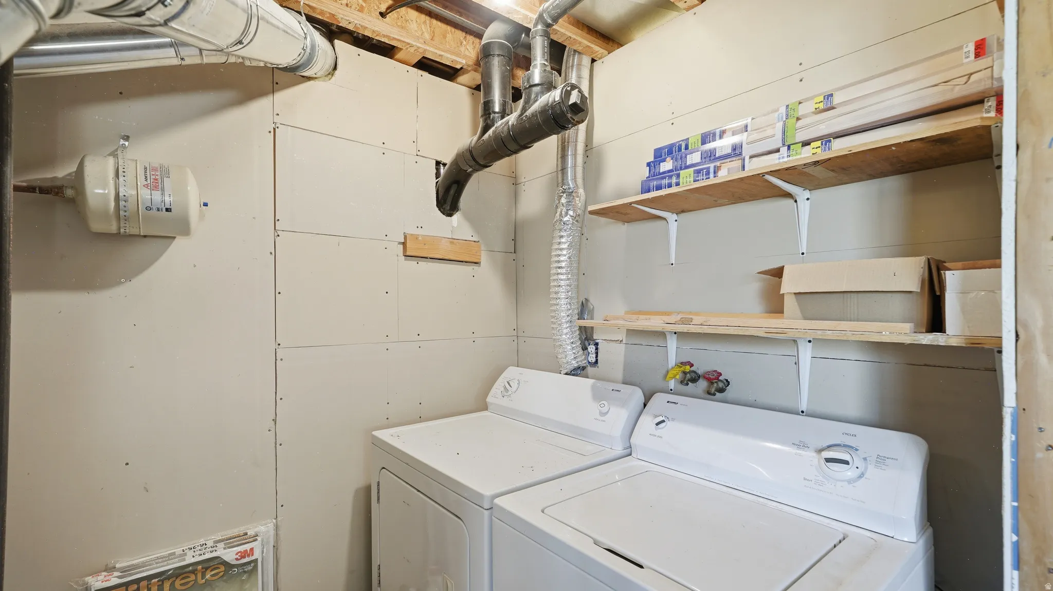 Dedicated utility space featuring a washer and dryer, exposed ductwork, and two wall-mounted storage shelves