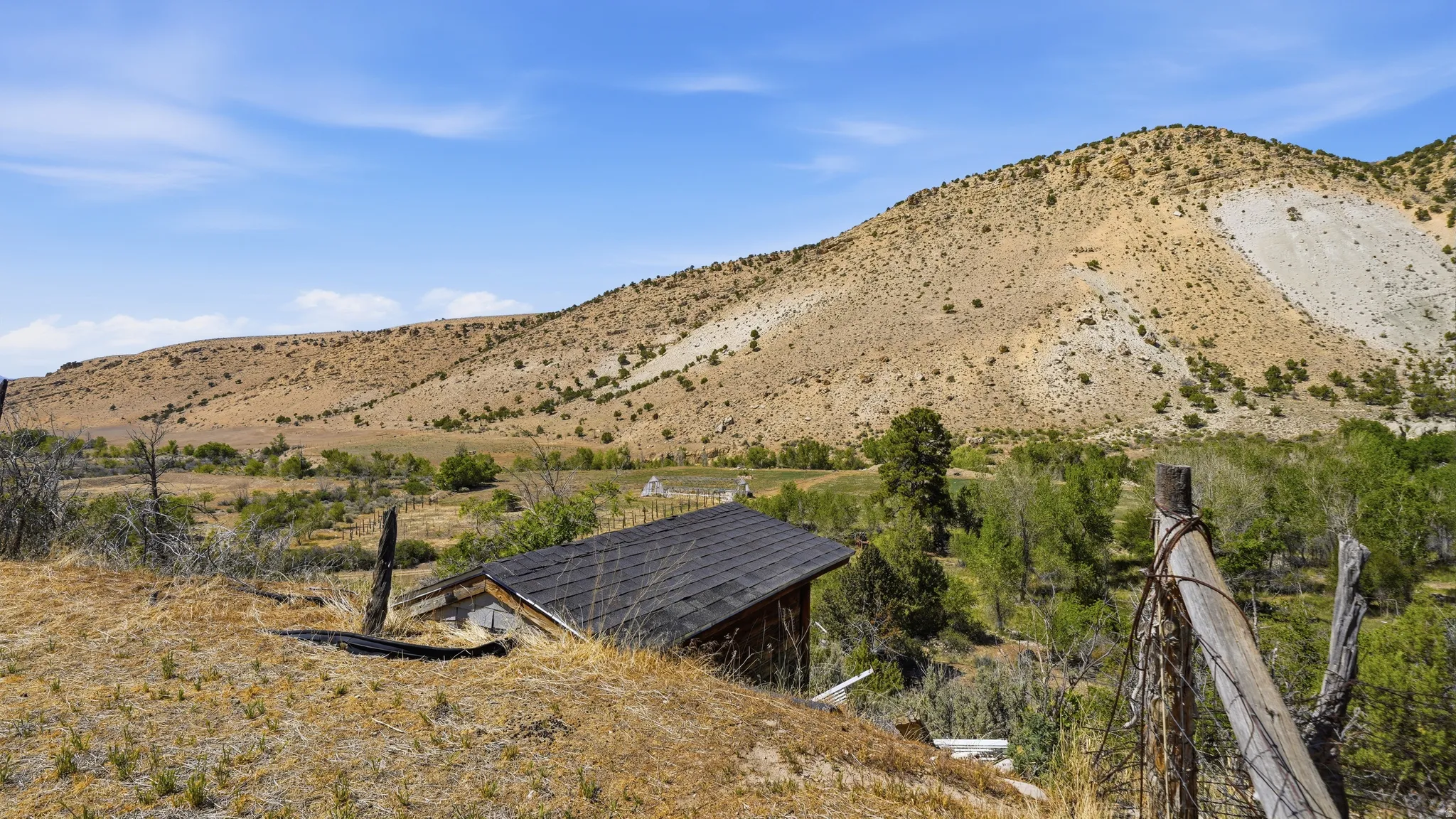 Expansive natural landscape featuring rolling hills, a valley with mature trees, and a clear blue sky