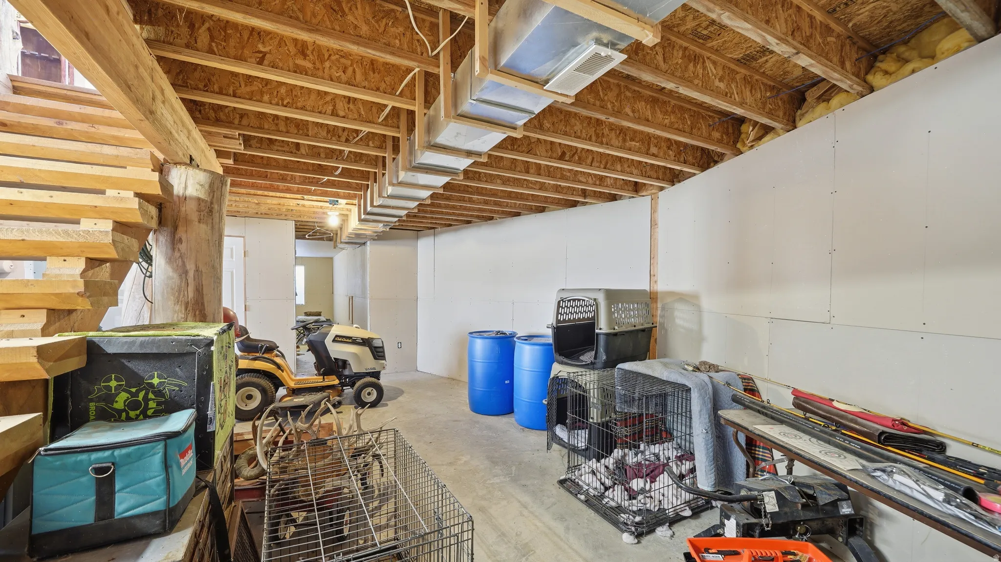 Unfinished basement space featuring exposed wooden ceiling joists, concrete flooring, and partial drywall installation on perimeter walls