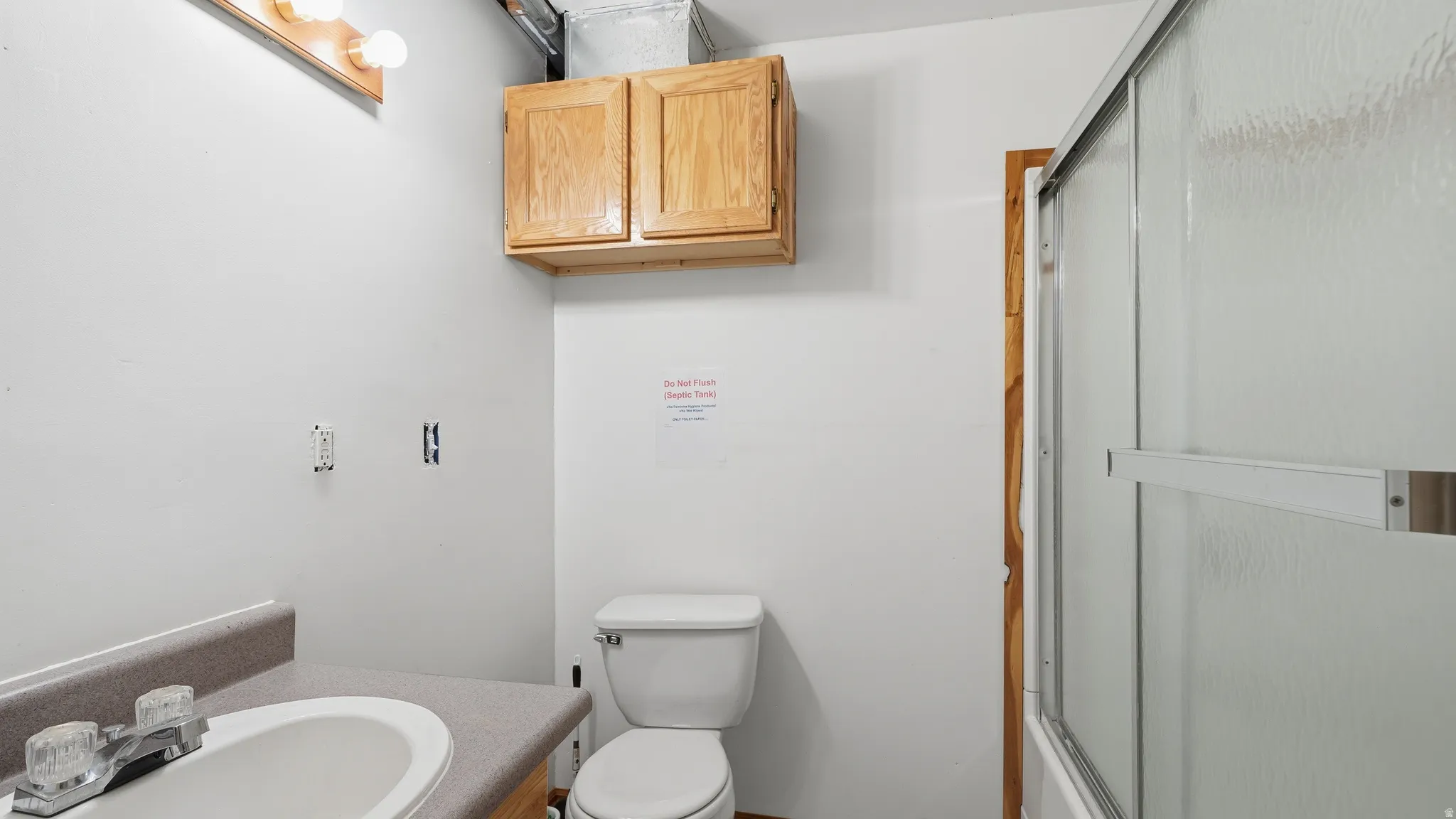 Bathroom featuring a white toilet, light wood-finish vanity with an integrated sink, a mounted light fixture, and a shower with sliding frosted glass doors