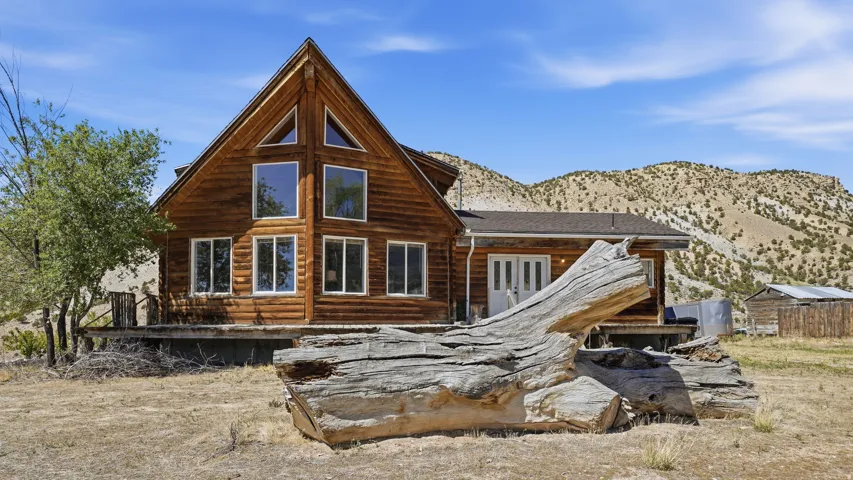 Log cabin exterior with a prominent A-frame architectural style, featuring multiple large windows and a gable roofline