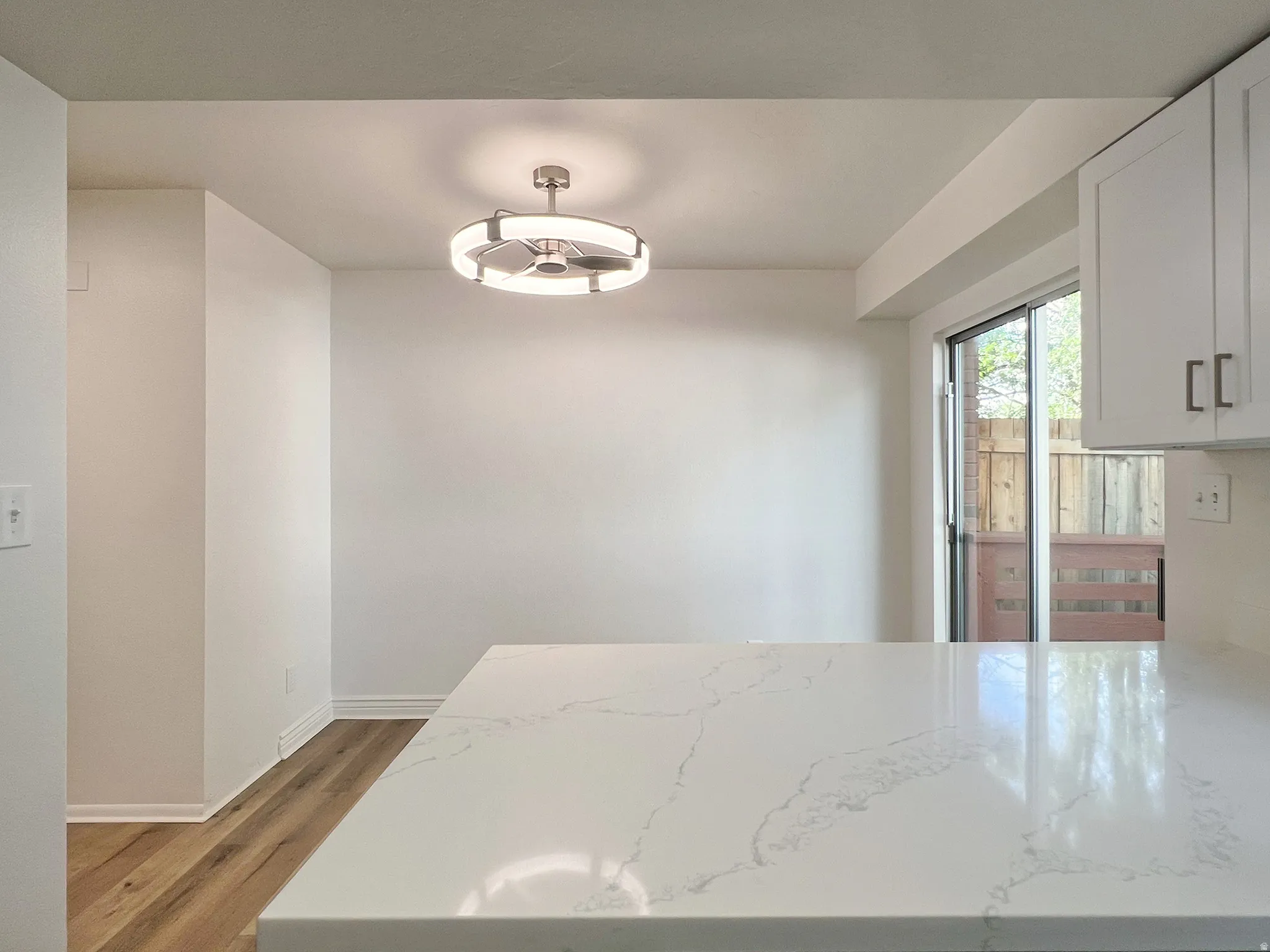White countertop with veining, wood-finish flooring, white cabinetry with silver hardware, recessed lighting, and a sliding glass door