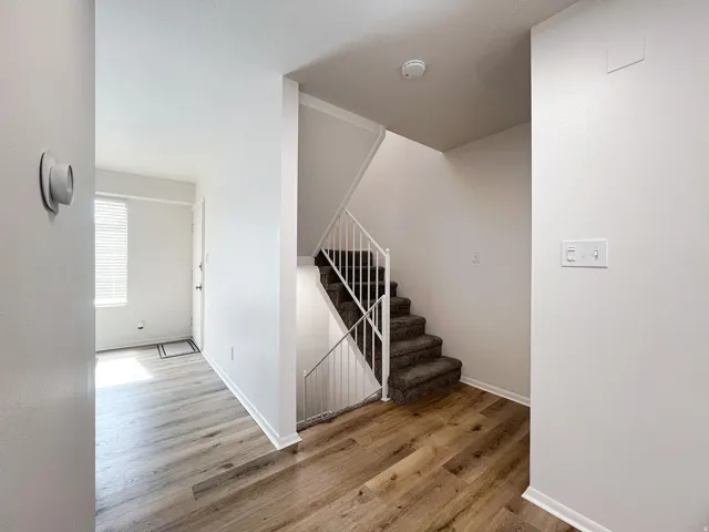 Interior entryway with wood-finish flooring, a carpeted staircase with white railings, and a window with blinds
