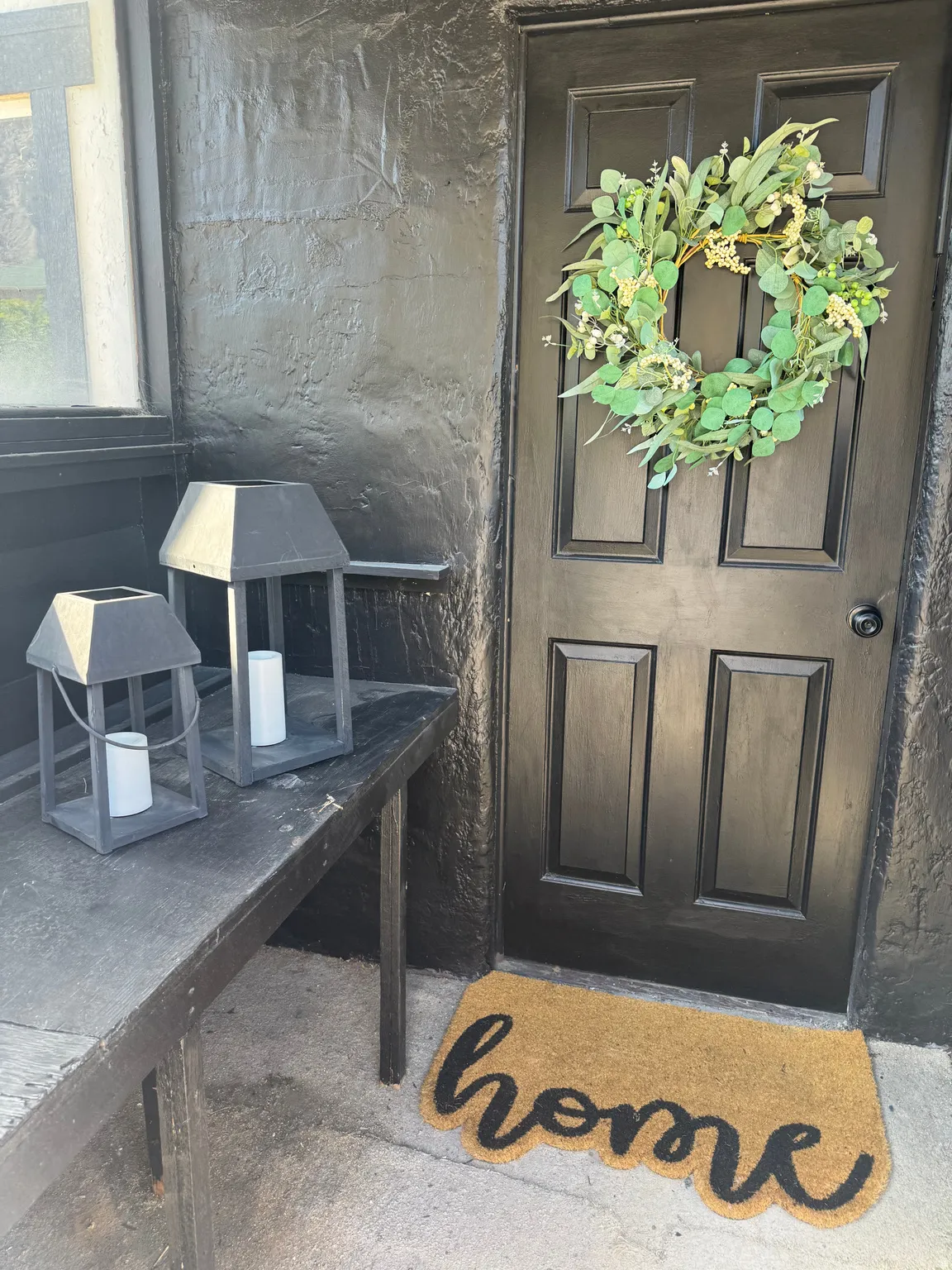 Dark paneled entry door with black hardware, complementing the textured black exterior wall