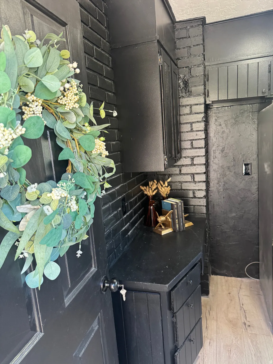 Black paneled door with round knob, contrasting with a black-painted brick wall