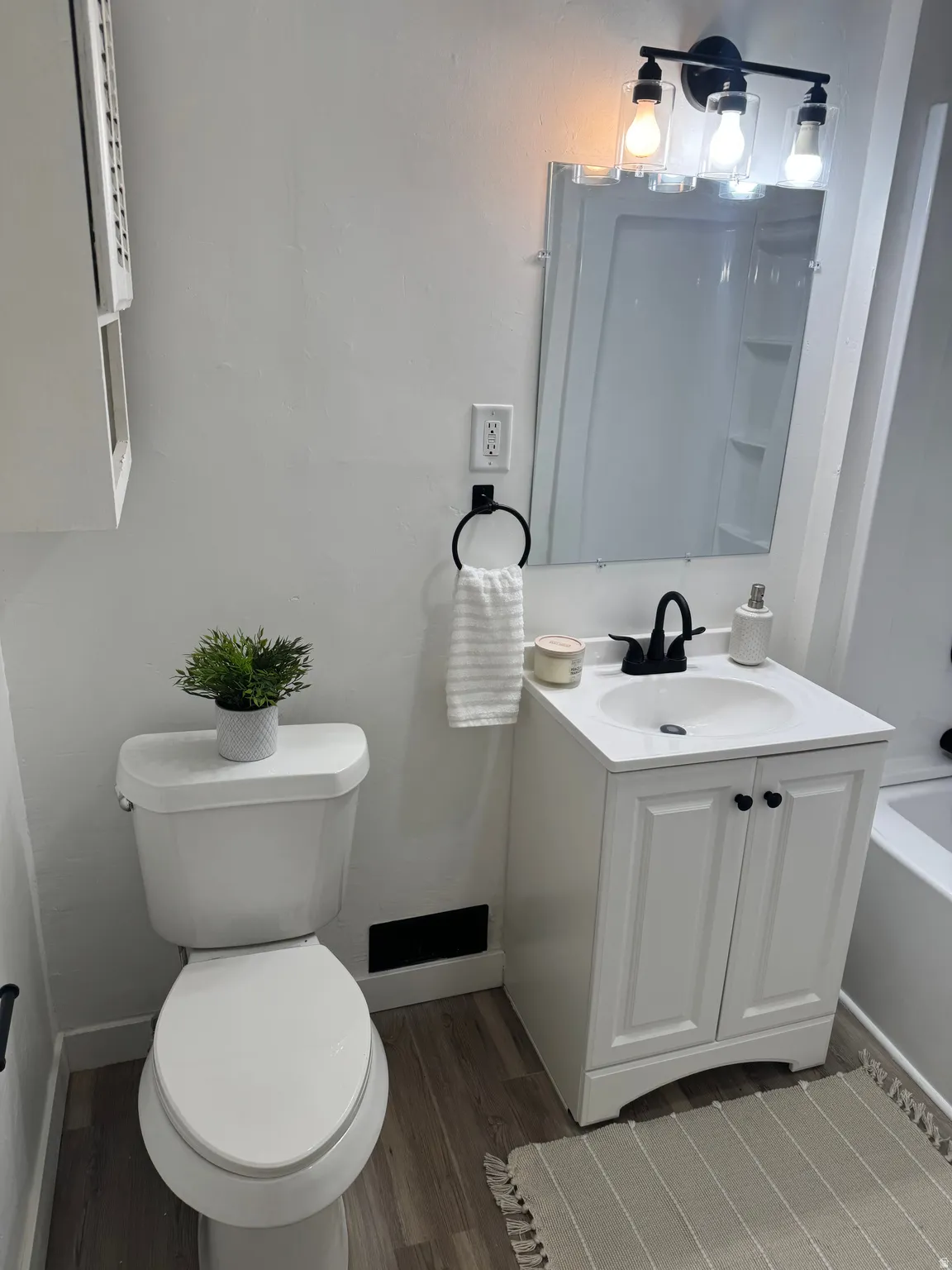 Bathroom featuring a white vanity with integrated sink, black matte faucet, and wood-finish flooring