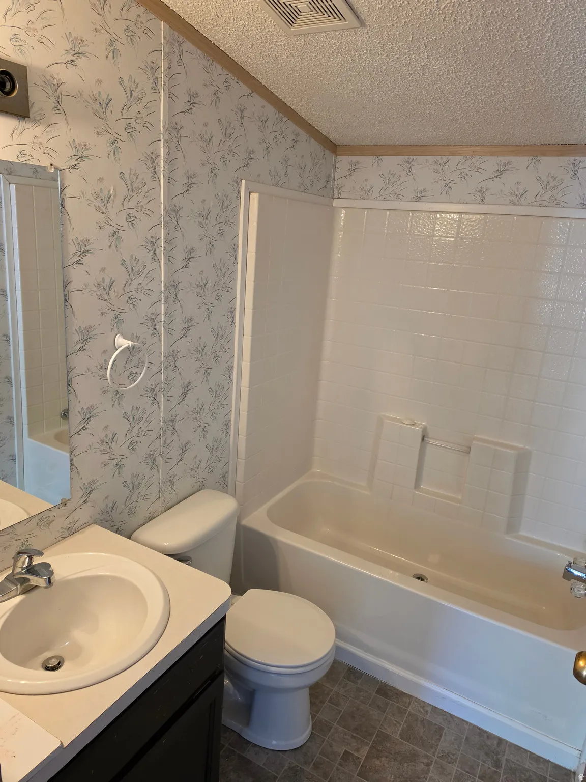 Bathroom featuring a white vanity with integrated sink, chrome faucet, white toilet, and a white bathtub with a tiled surround