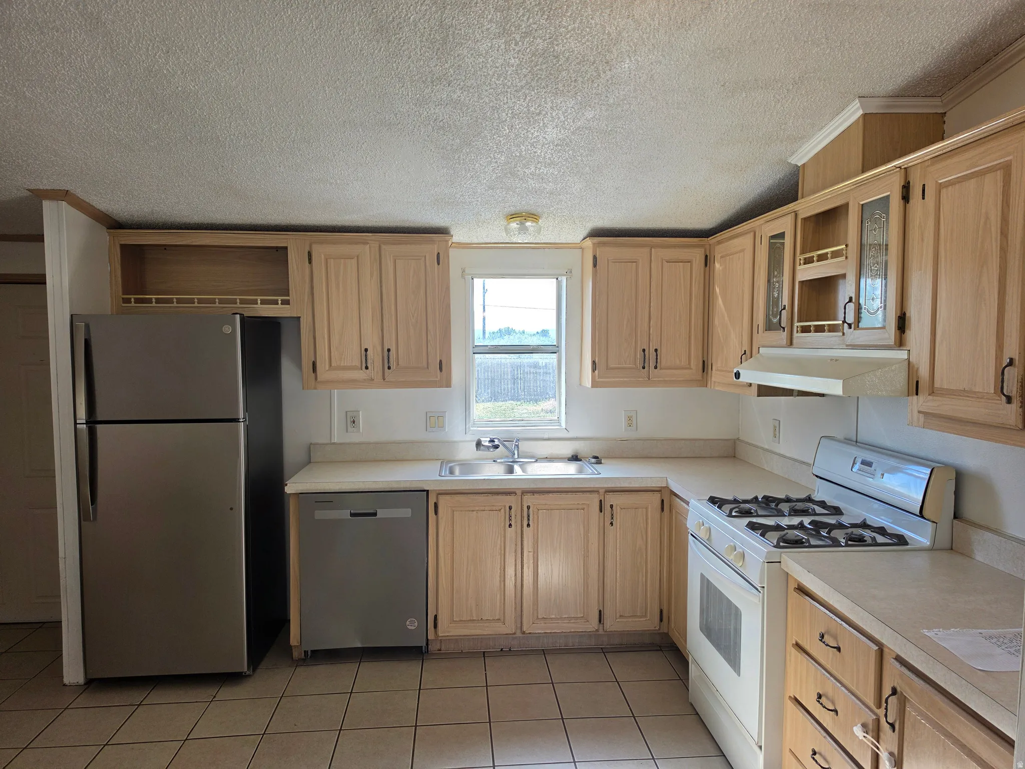 Kitchen featuring light wood-finish cabinetry, a stainless steel refrigerator, a gas range, a built-in dishwasher, and a double basin sink