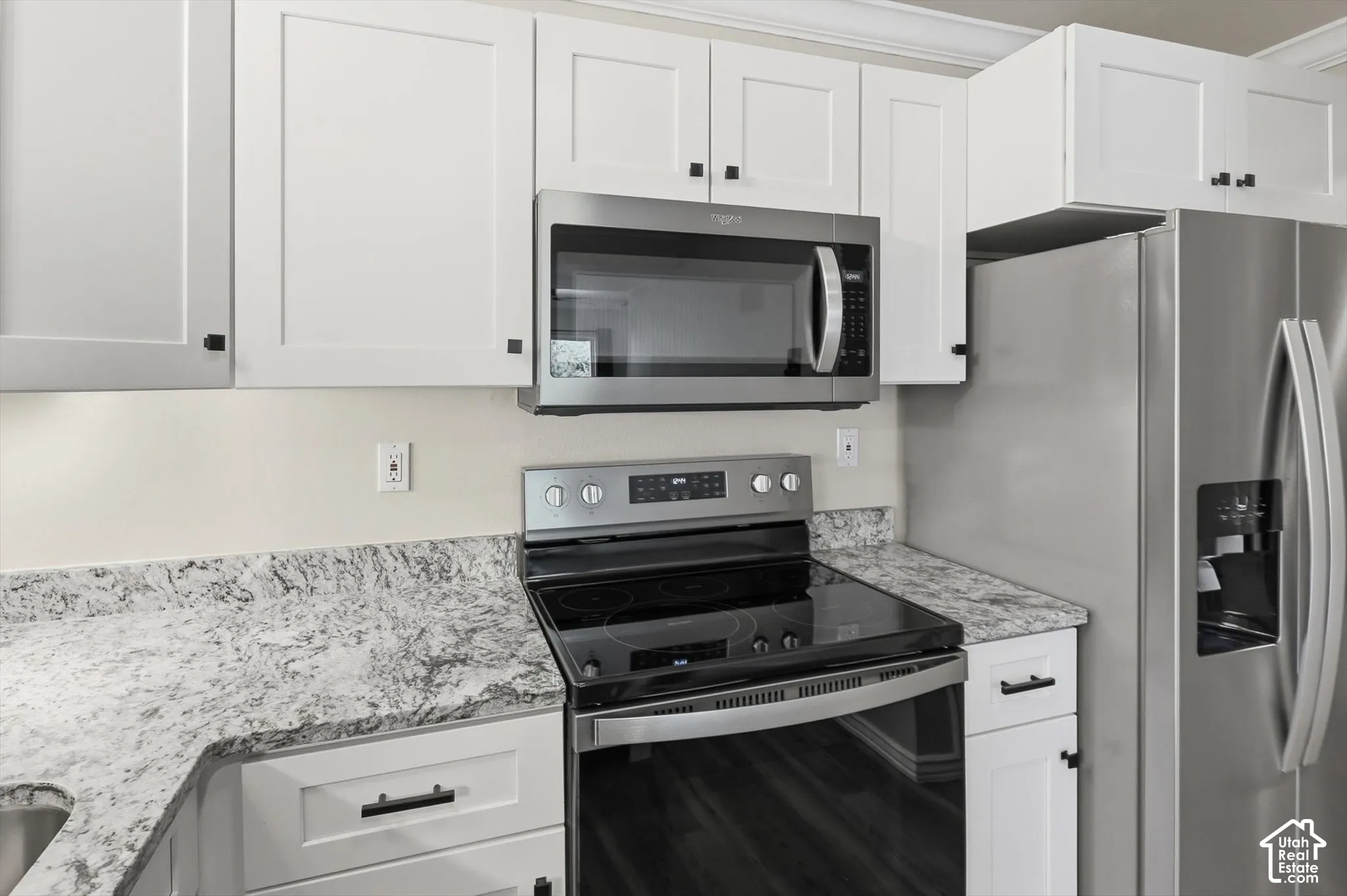 Kitchen featuring white shaker-style cabinetry, stainless steel appliances, speckled countertops, and wood-finish flooring