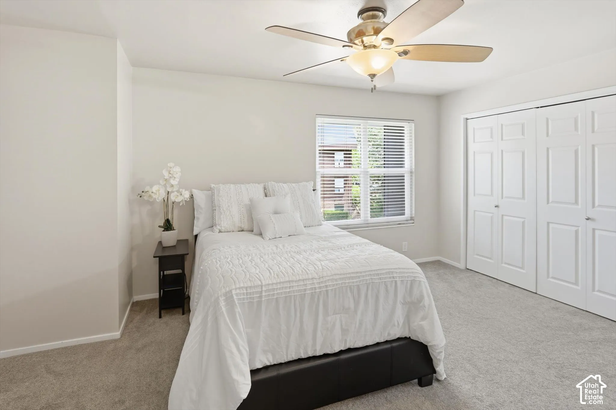 Bright bedroom featuring light gray carpeting, a window with horizontal blinds, and a ceiling fan with integrated lighting