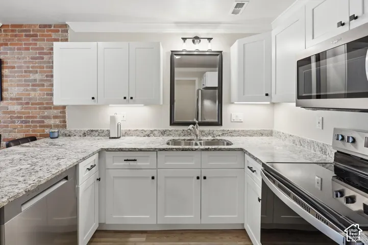 U-shaped kitchen featuring white shaker cabinetry, speckled countertops, a stainless steel sink, and exposed brick detailing