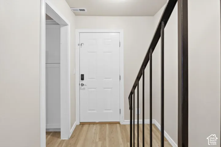 Front door with smart lock, wood-finish flooring, and a dark metal staircase railing