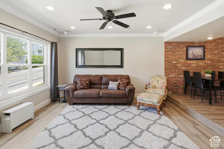Spacious living area featuring light wood-finish flooring, a contemporary ceiling fan, recessed lighting, and crown molding