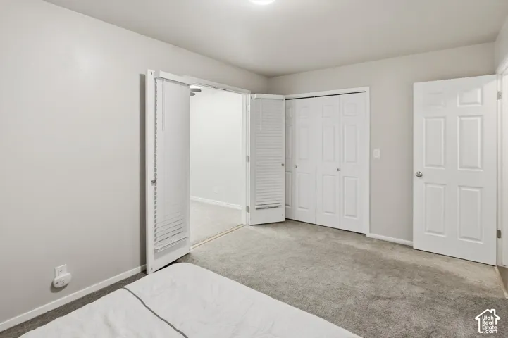 Carpeted room with light grey walls, featuring a bi-fold closet with louvered doors, a six-panel door, and a separate bi-fold closet