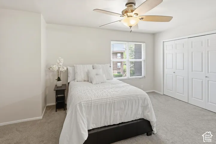 Bright bedroom featuring light gray carpeting, a window with horizontal blinds, and a ceiling fan with integrated lighting
