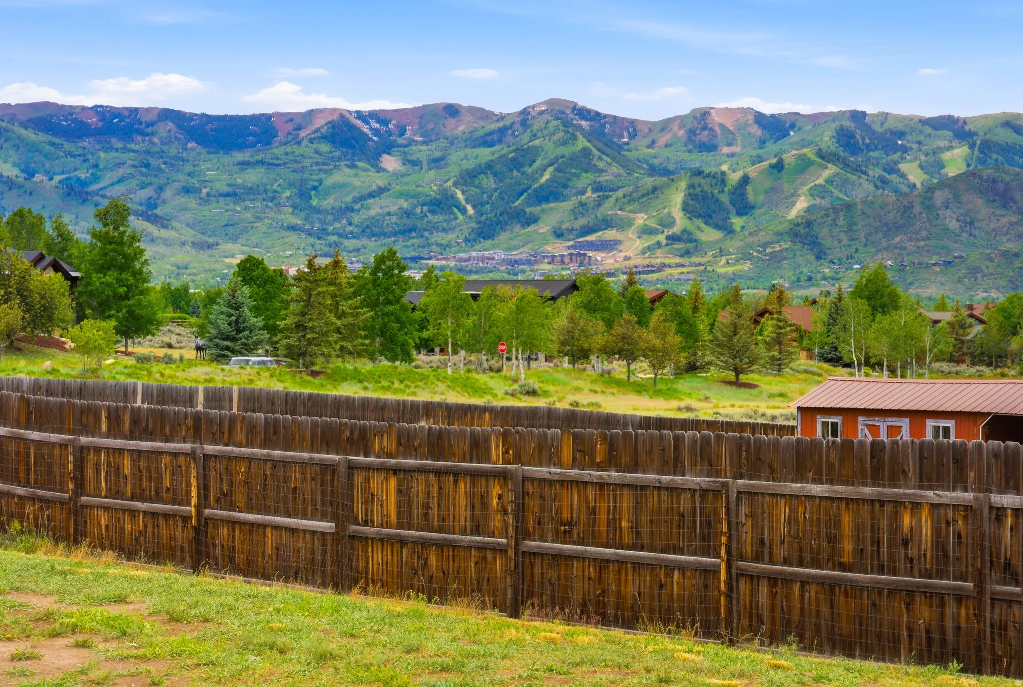 Wood privacy fence enclosing a grassy property, with a red outbuilding featuring a brown metal roof
