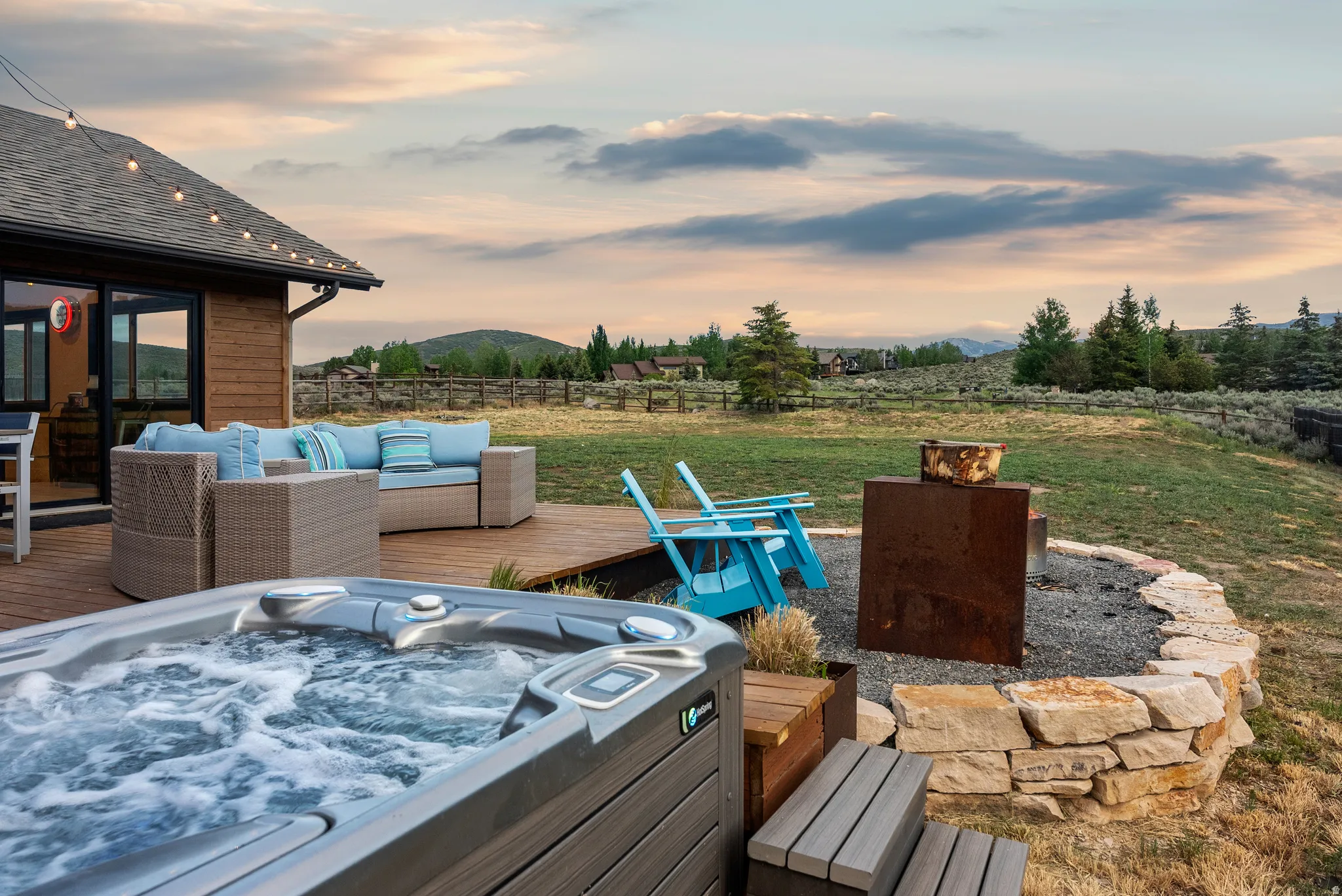 Outdoor spa area featuring a built-in hot tub, a stone-lined fire pit, and a wooden deck