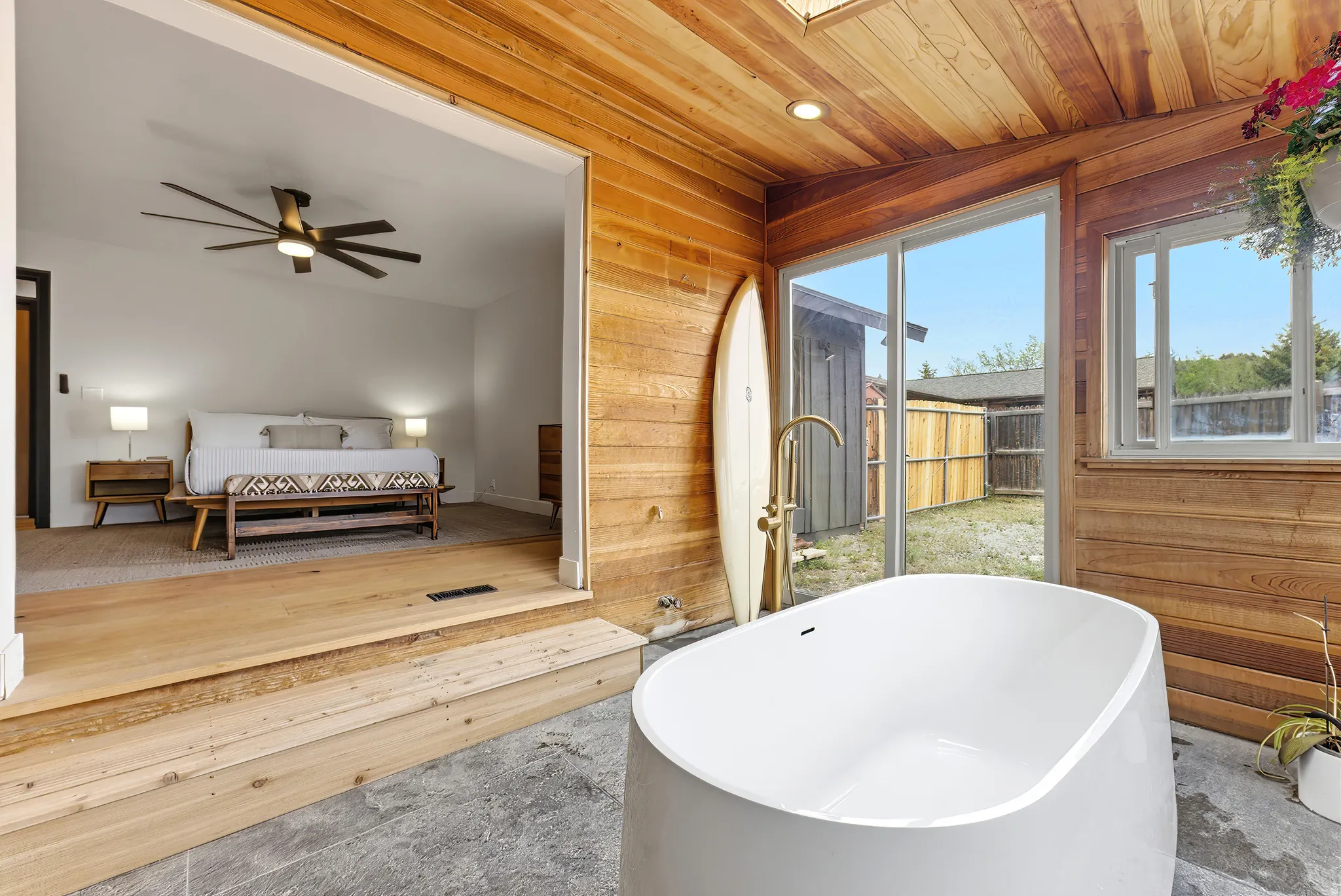 Freestanding soaking tub with a floor-mounted gold-tone faucet, wood-paneled walls and ceiling, skylight, and large sliding glass door