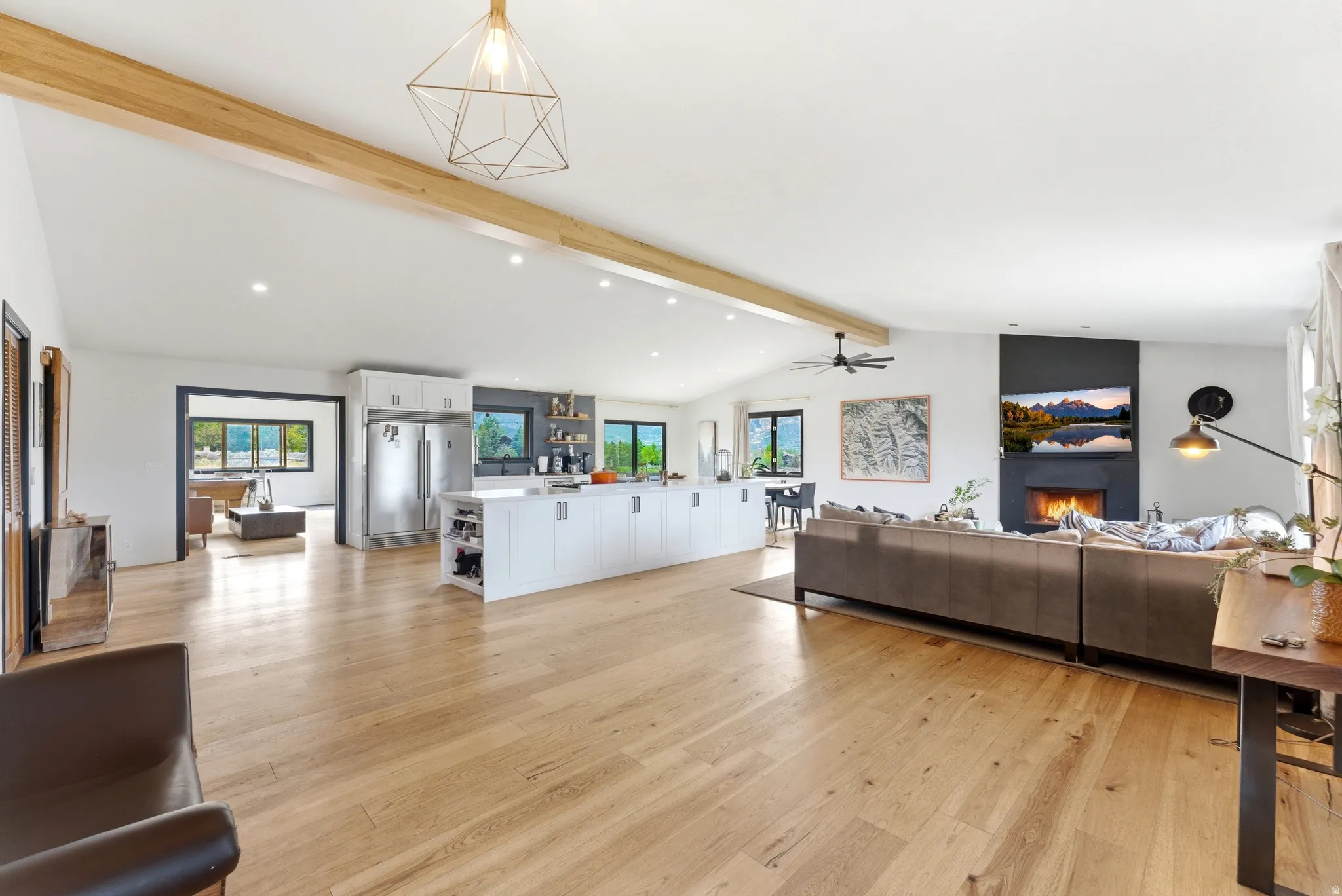 Spacious open-concept living area featuring light wood-finish flooring, vaulted ceilings with exposed wood beams, and recessed lighting