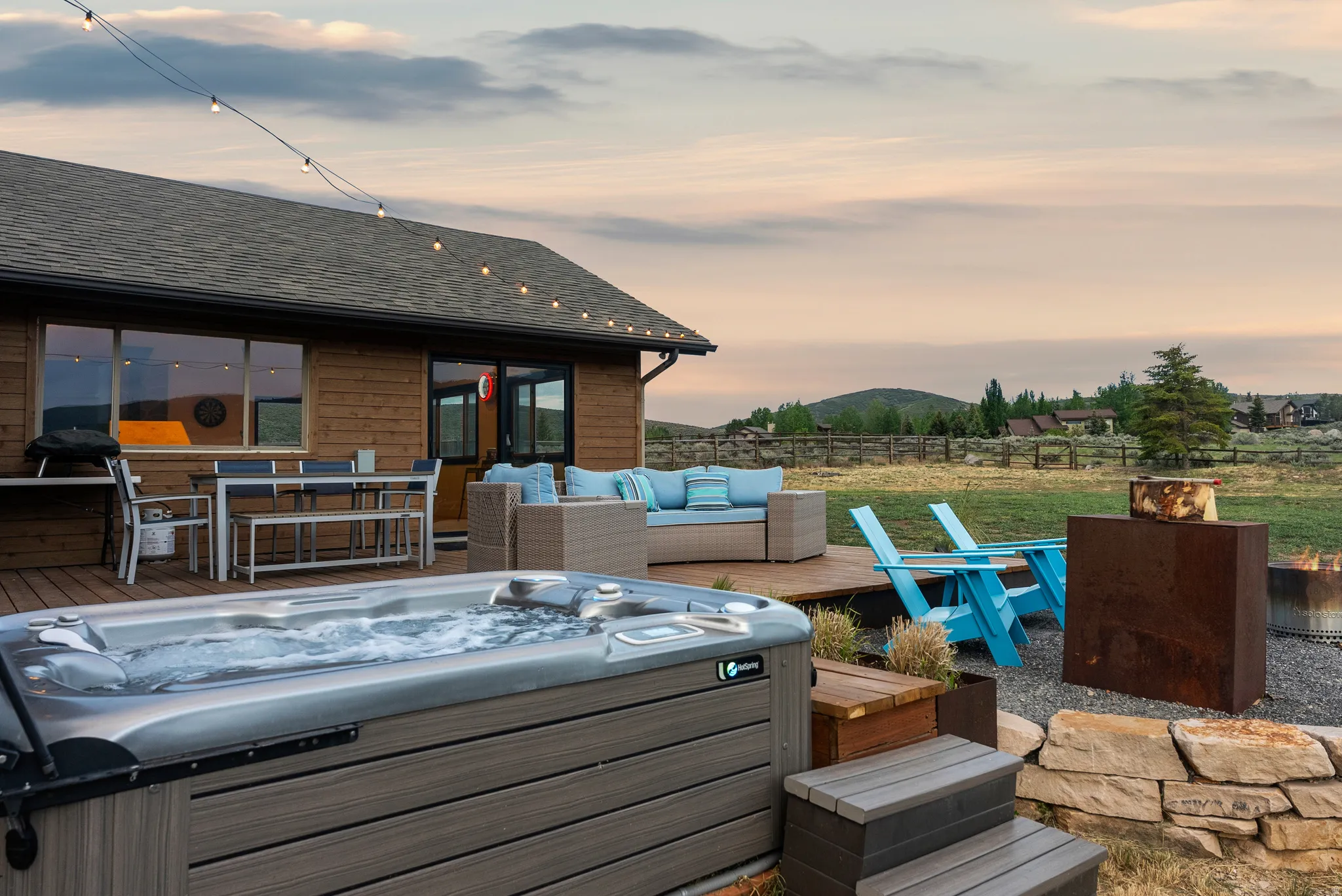 Exterior hot tub and expansive wood-finish deck with string lighting