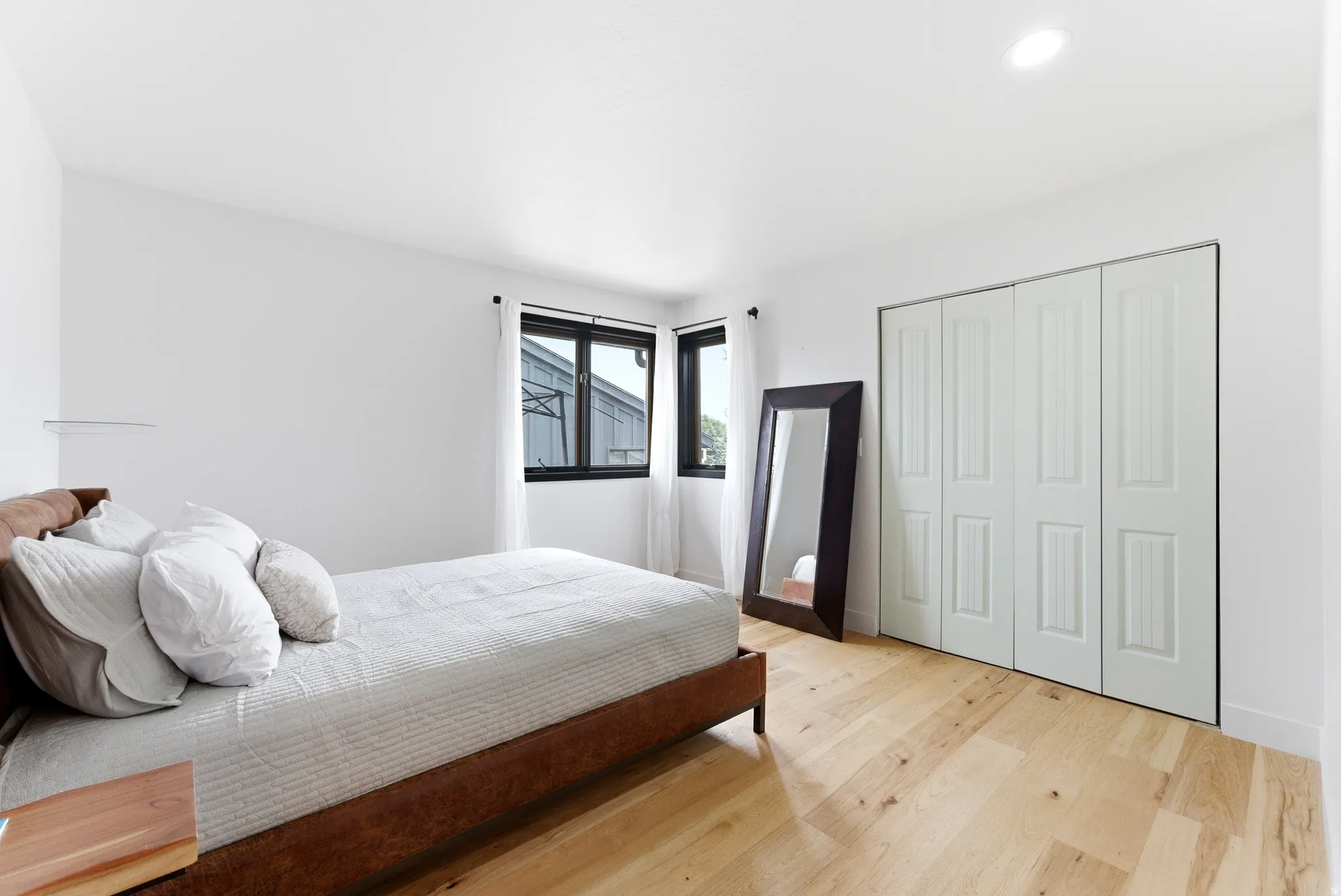 Bright interior with wood-finish flooring, featuring a large built-in closet with bi-fold doors, recessed lighting, and a corner window with dark framing