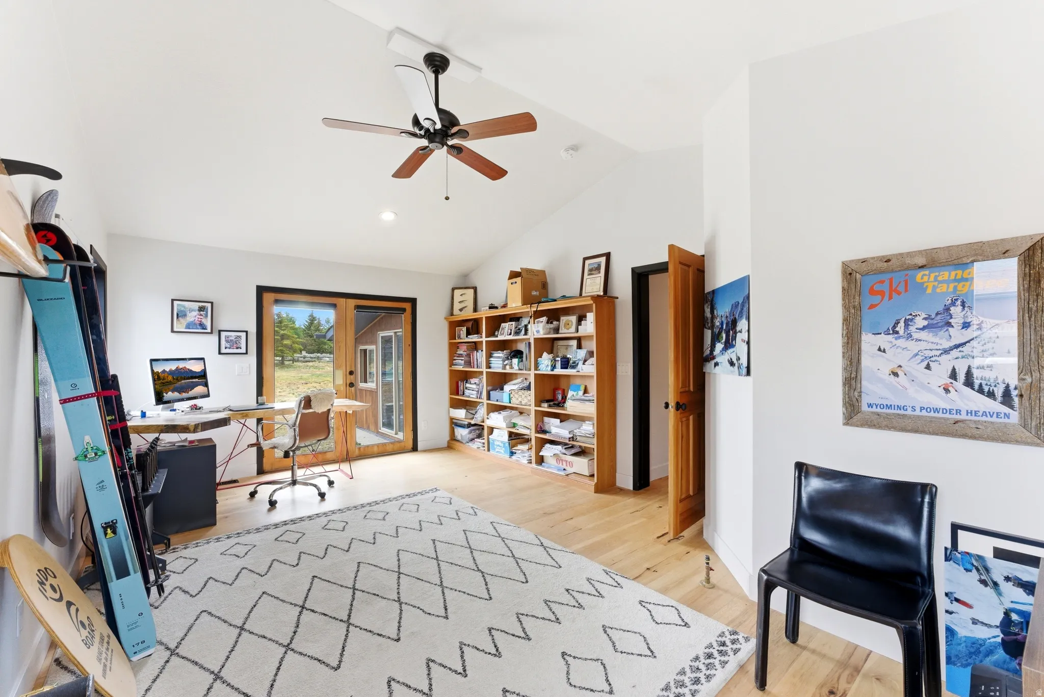Vaulted ceiling with a ceiling fan, light wood-finish flooring, built-in shelving, and French doors providing natural light
