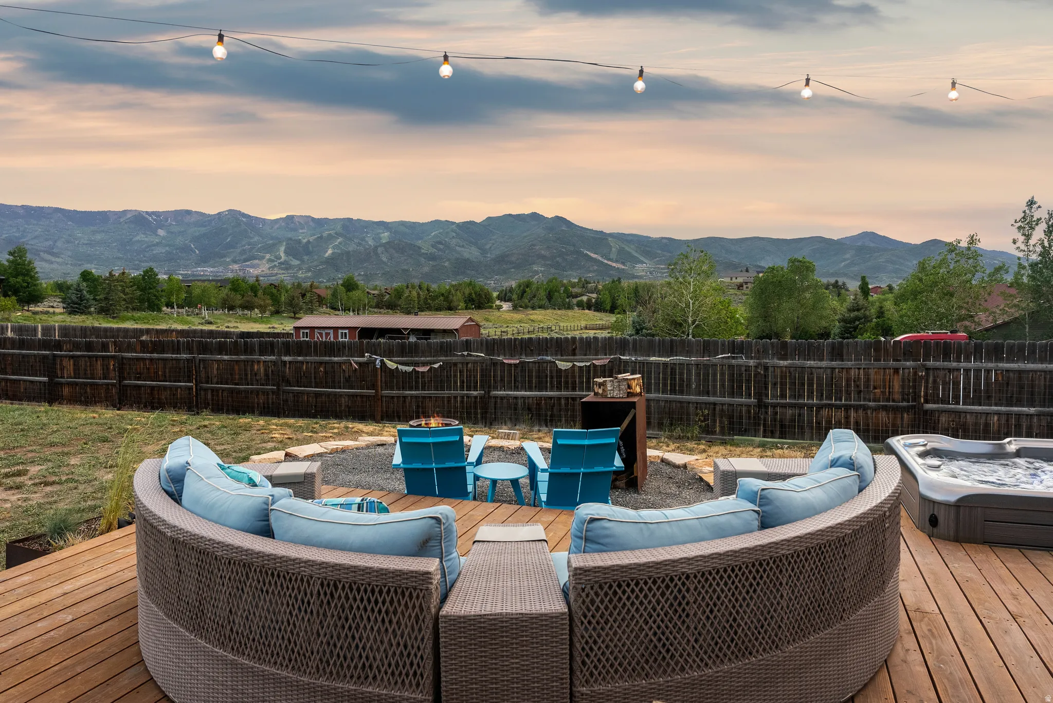 Expansive wood-finish deck featuring a hot tub and a separate gravel patio with a built-in fire pit
