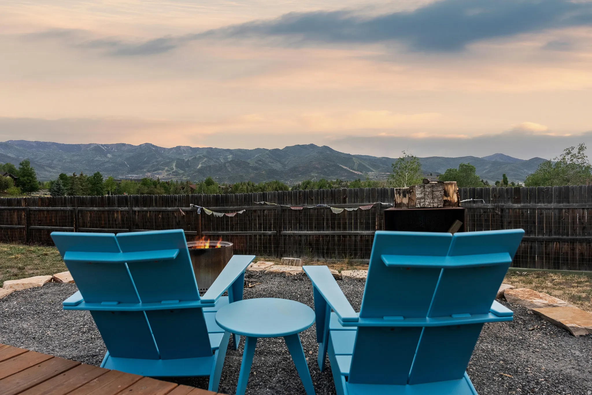 Outdoor fire pit area featuring a gravel surface, stone accents, and a wood fence border
