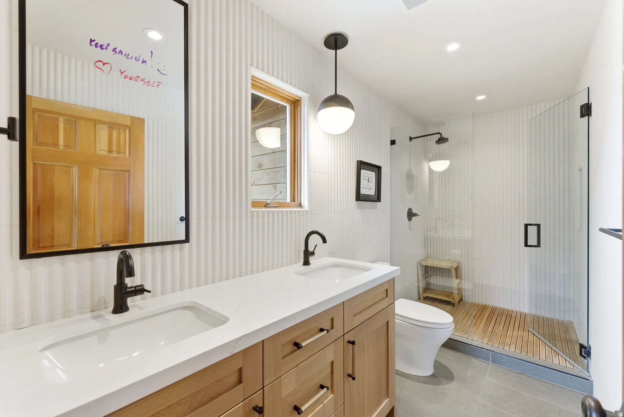 Bathroom featuring a dual-sink vanity with light wood cabinetry and a white countertop