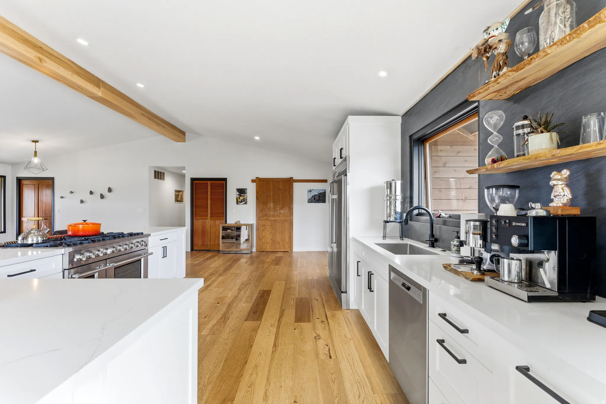 Open-concept kitchen featuring white cabinetry, stainless steel appliances, a large range with multiple burners, wood-finish flooring, and exposed ceiling beams