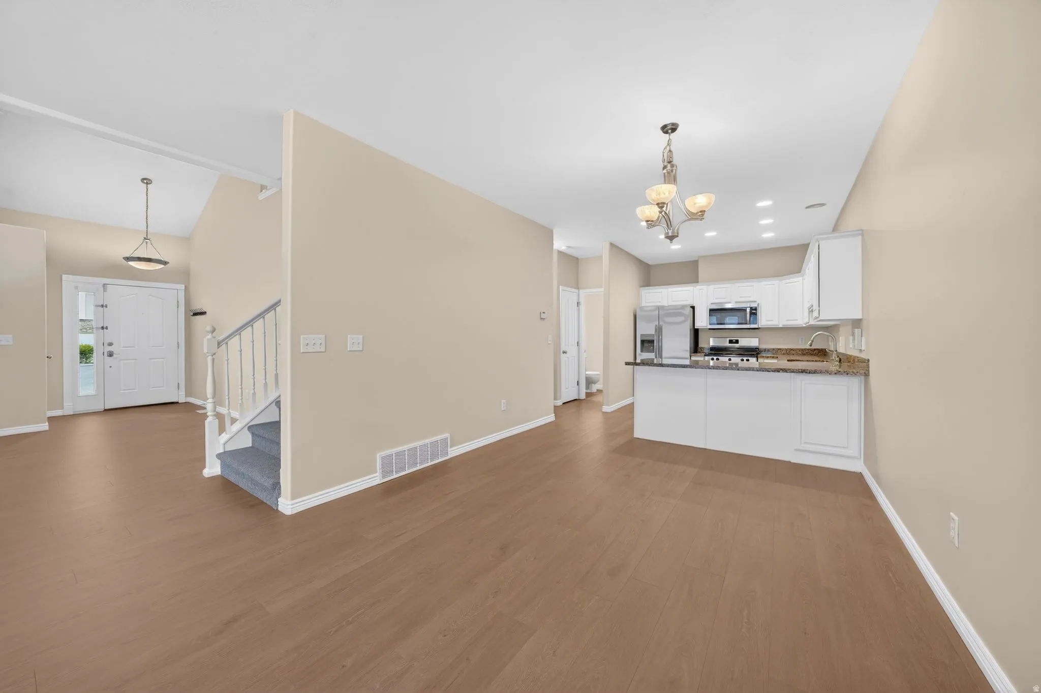 Open-concept living space featuring wood-finish flooring, a kitchen with white cabinetry and granite countertops, and a staircase with carpeted treads