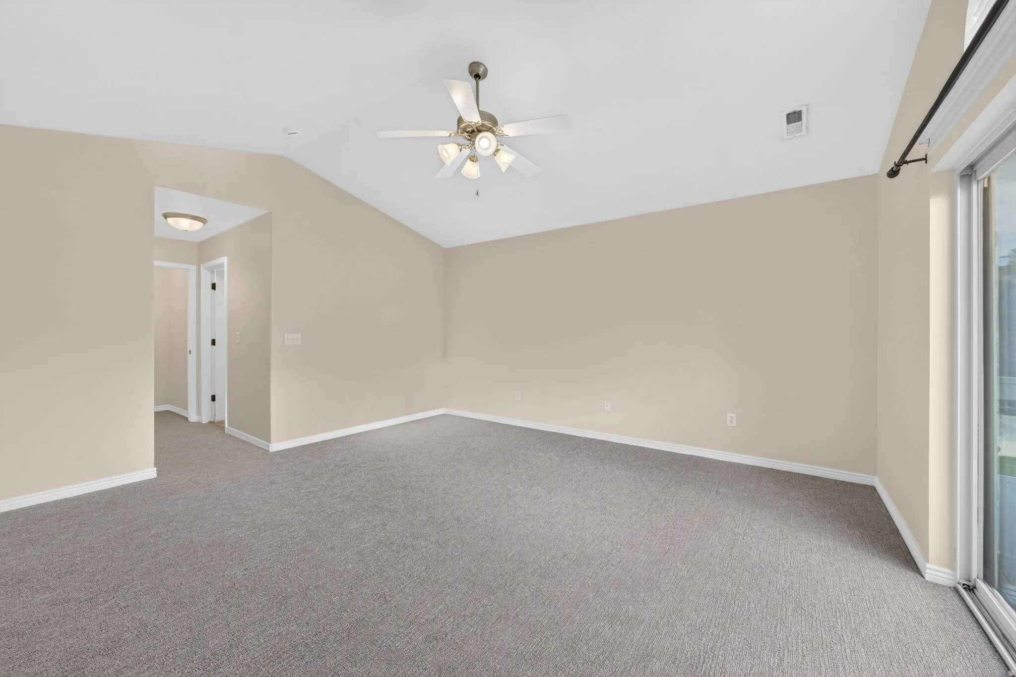 Carpeted room featuring vaulted ceilings, a ceiling fan with light fixture, neutral wall paint, and white baseboards