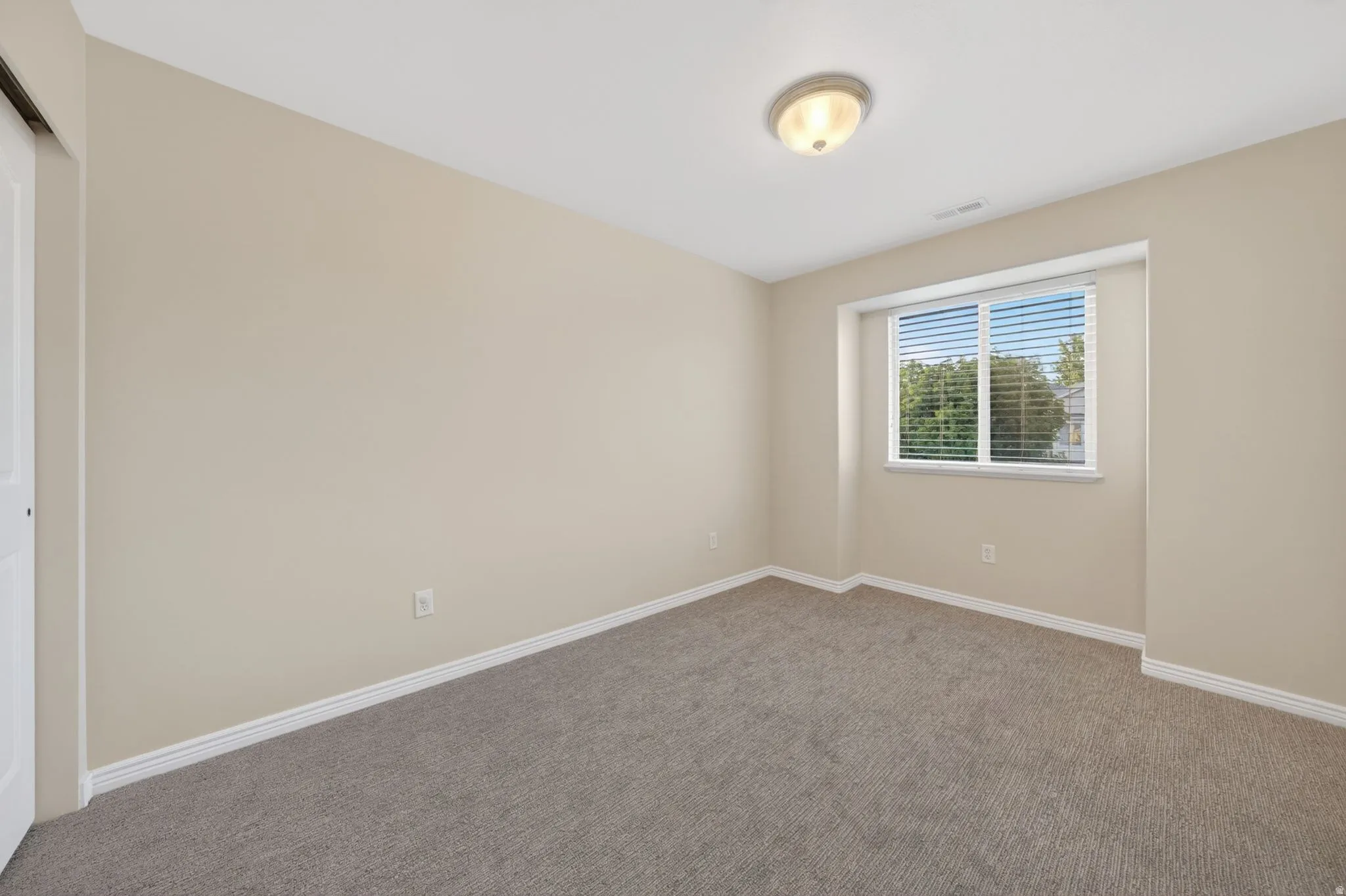 Carpeted room featuring neutral wall tones, white baseboards, and a window with blinds