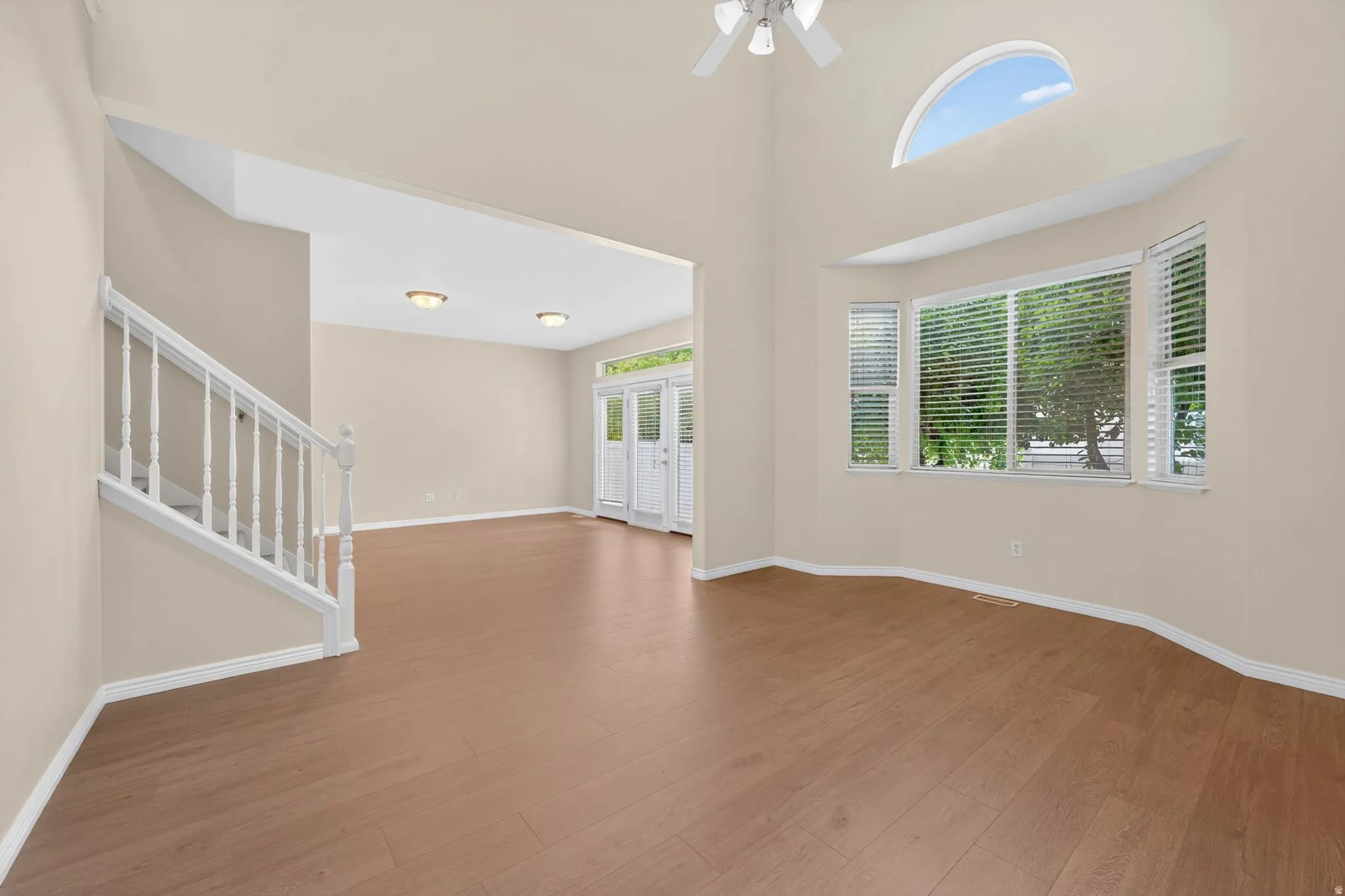 Spacious living area featuring wood-finish flooring, a bay window with blinds, and a vaulted ceiling with a fan