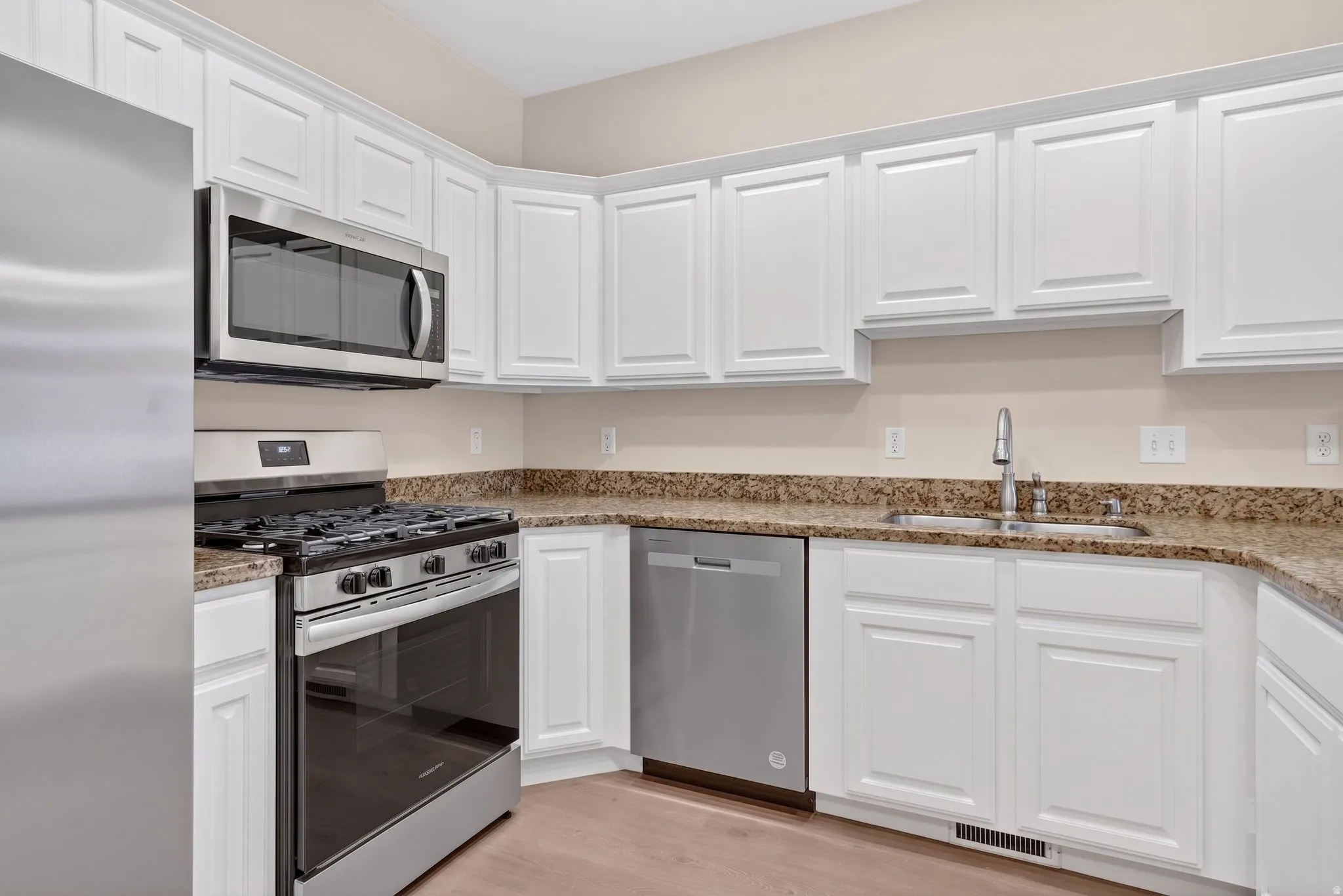Modern kitchen featuring white cabinetry, granite countertops, and stainless steel appliances including a gas range, microwave, and dishwasher