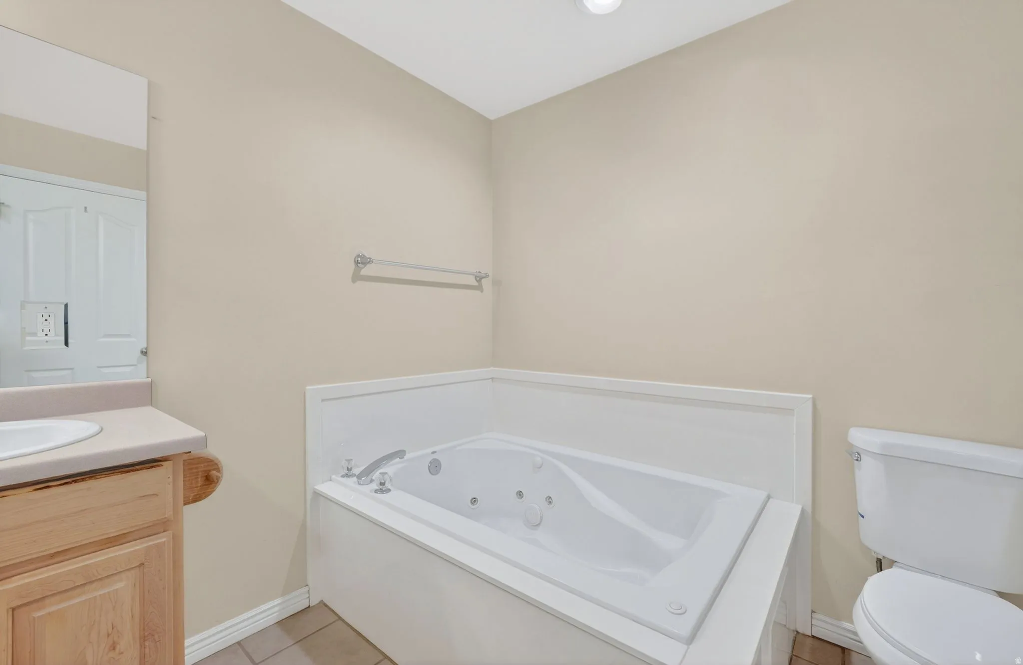 Soaking tub with integrated jets, neutral wall paint, recessed lighting, wood-finish vanity with countertop, and tile flooring