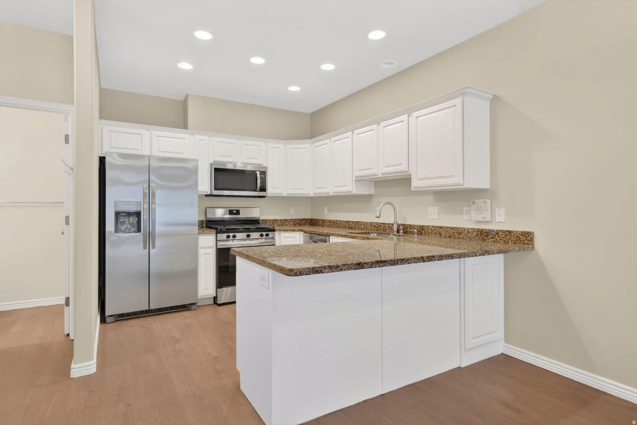 Kitchen featuring white cabinetry, stainless steel appliances, speckled stone countertops, and wood-finish flooring