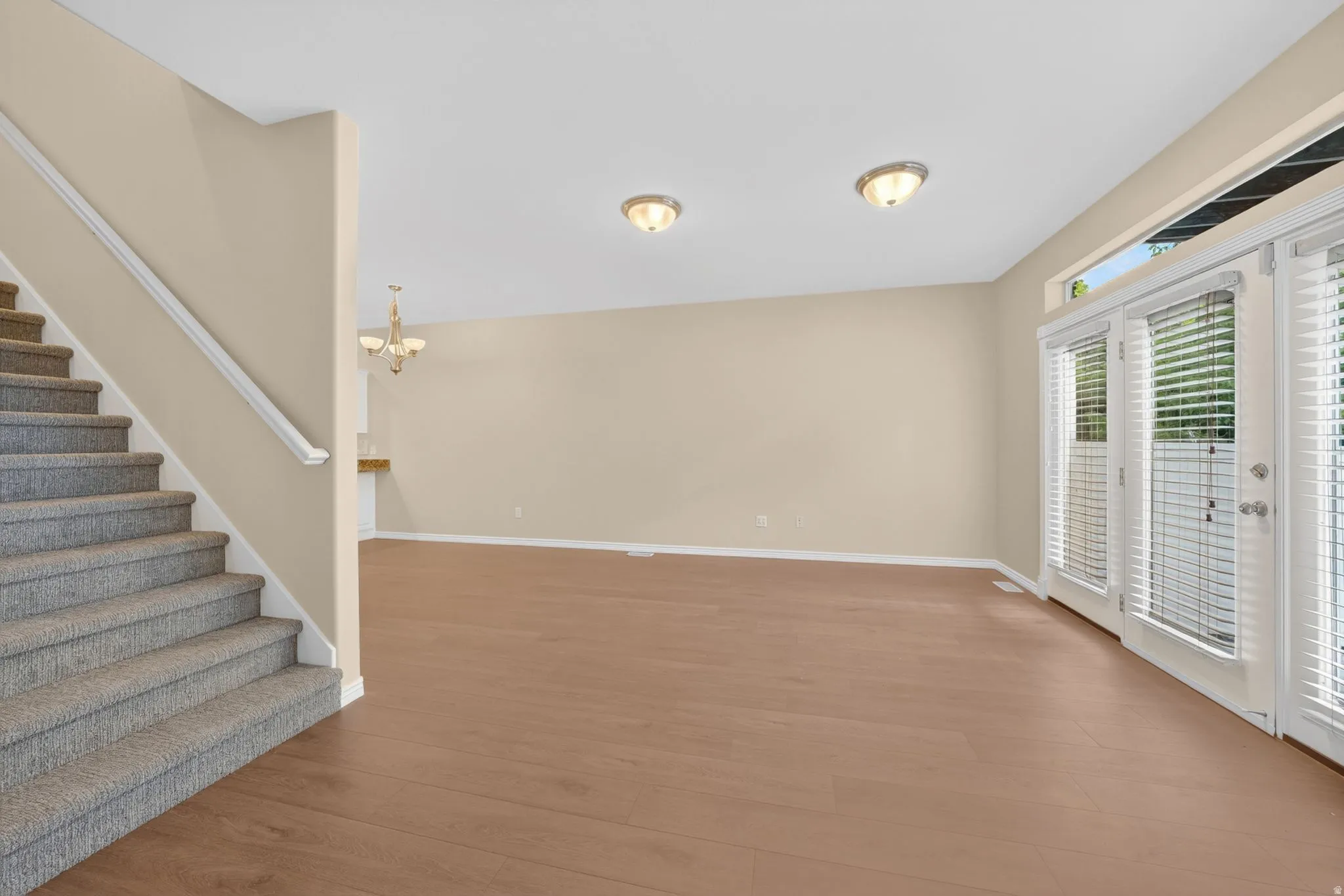 Spacious interior featuring wood-finish flooring, neutral paint tones, and a carpeted staircase with white railing
