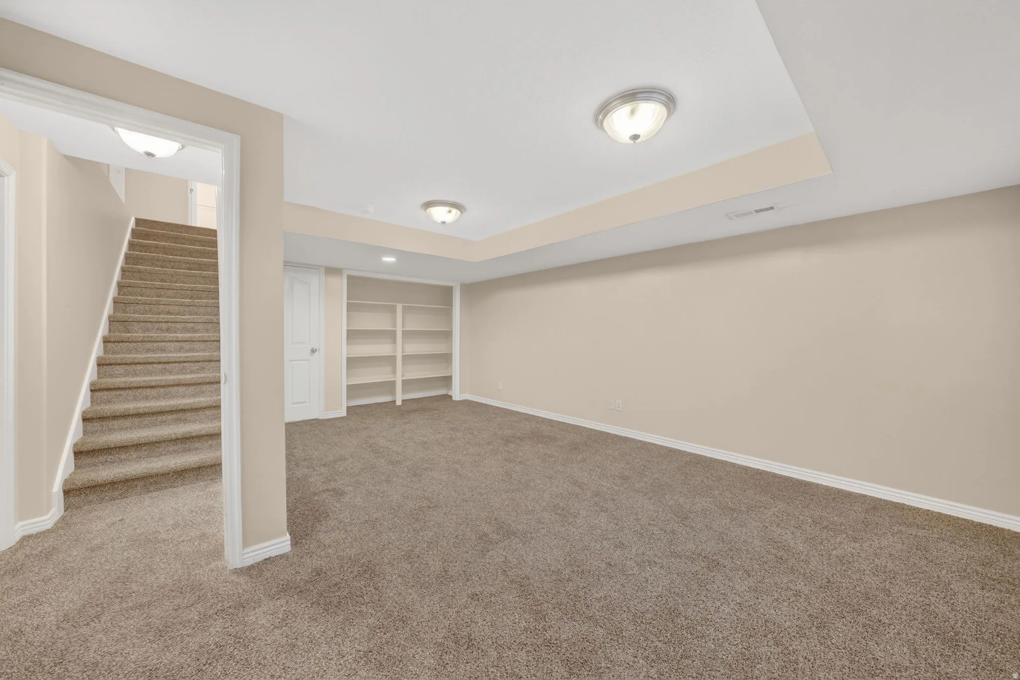 Spacious carpeted room featuring built-in shelving, tray ceiling, and recessed lighting
