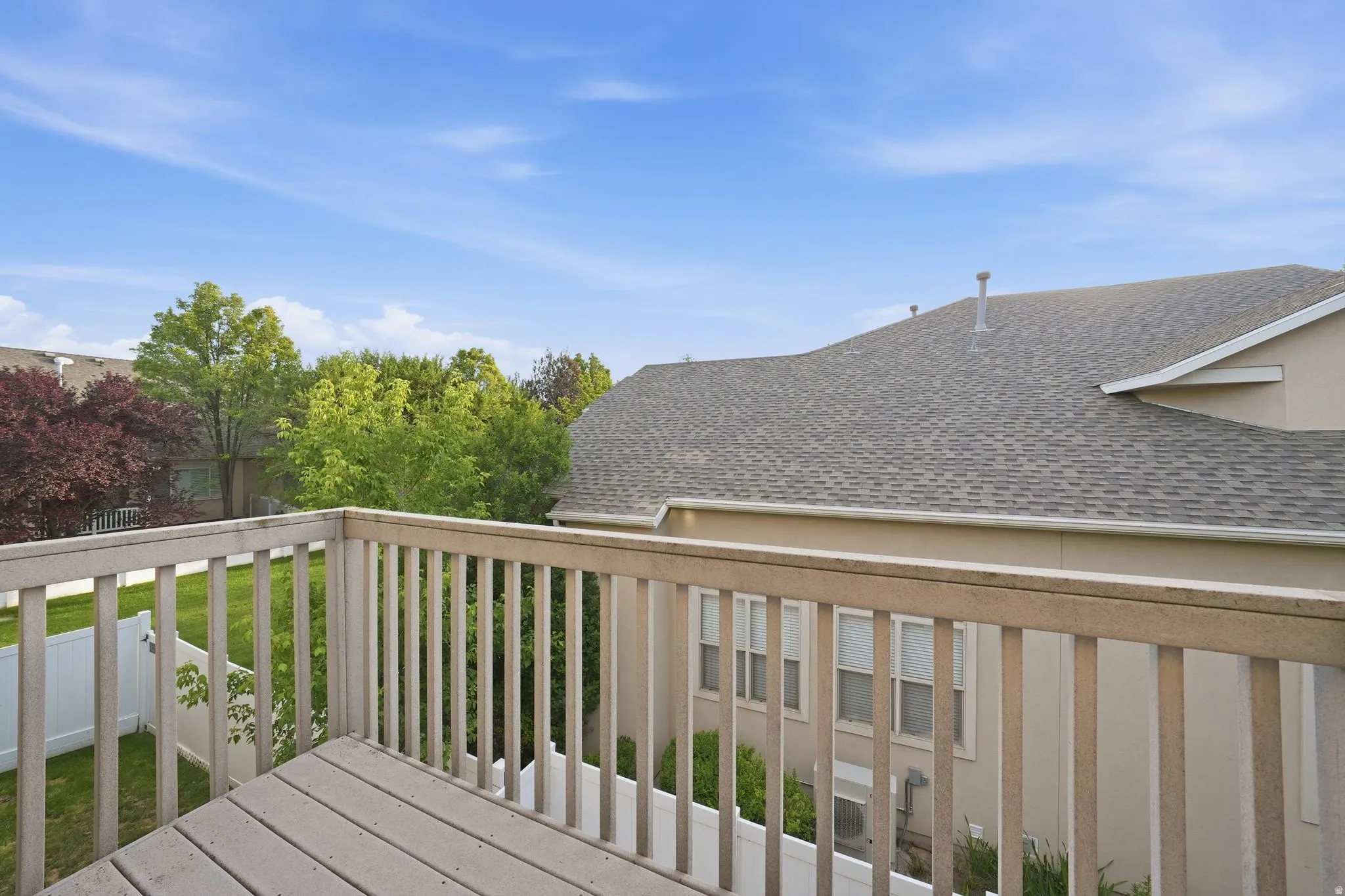 Outdoor deck with wood railings and deck boards, overlooking a green lawn and mature trees
