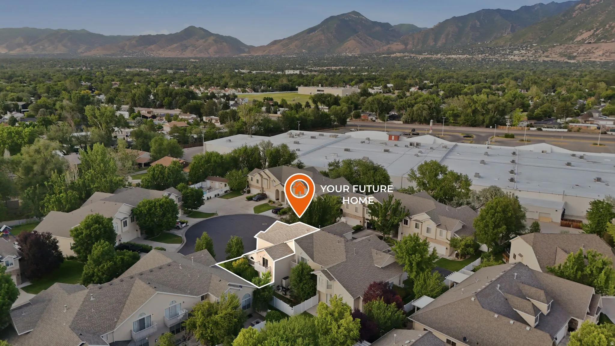 Aerial view featuring a residential area with mature trees and mountain backdrop