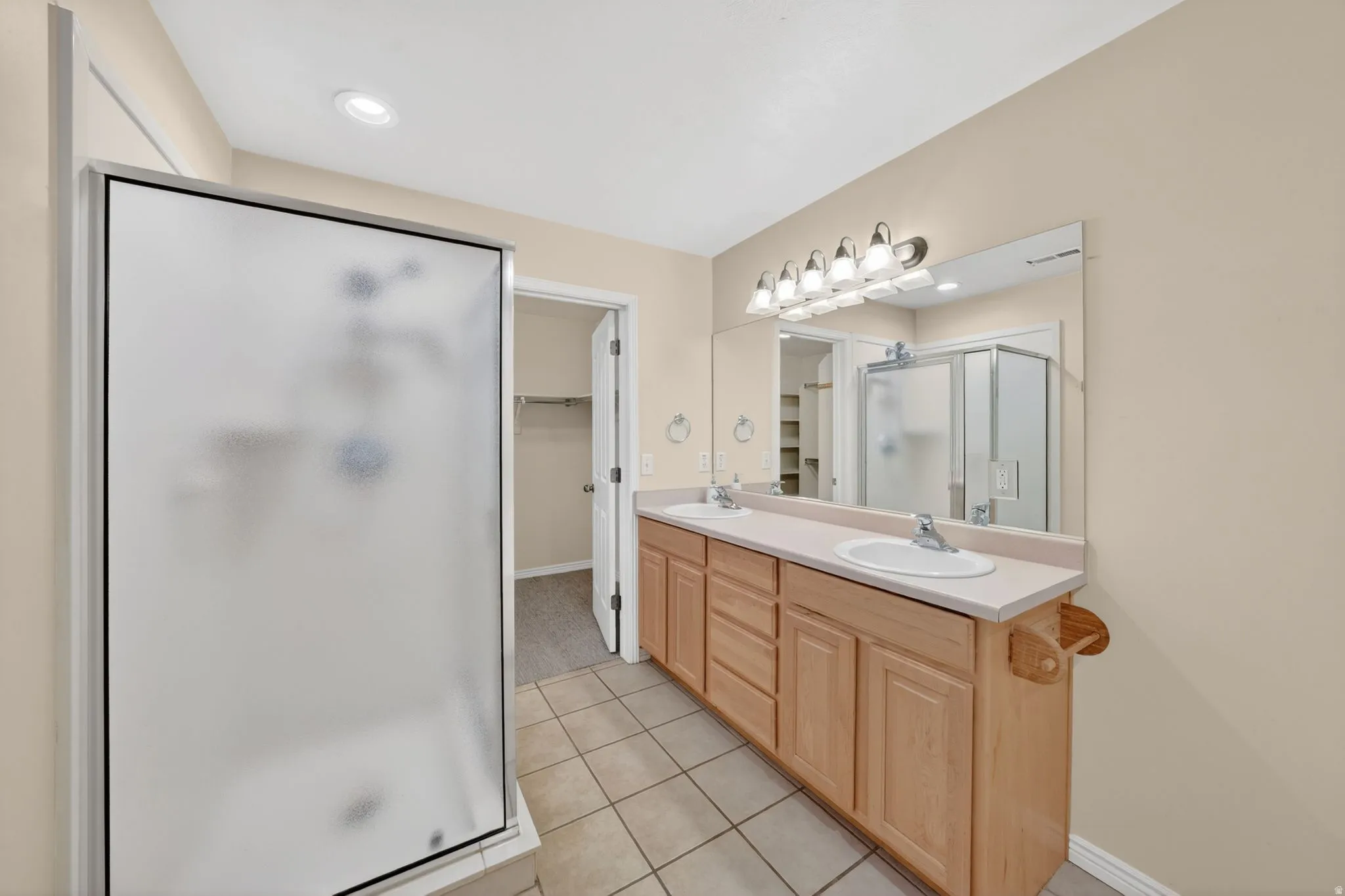 Bathroom featuring a double vanity with light wood cabinetry, dual sinks, and an expansive mirror