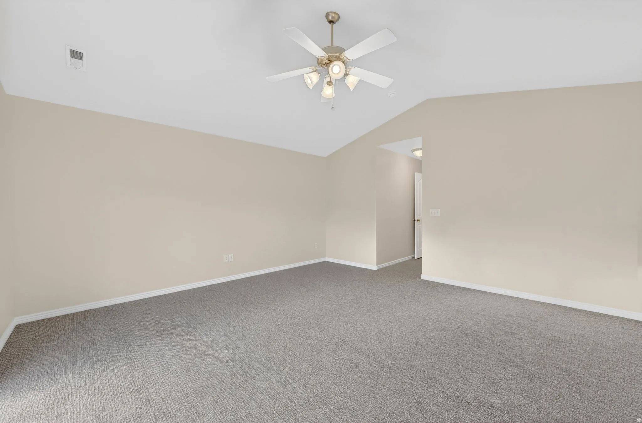 Spacious room featuring vaulted ceilings, light neutral wall paint, gray carpet flooring, white baseboards, and a ceiling fan with integrated lighting