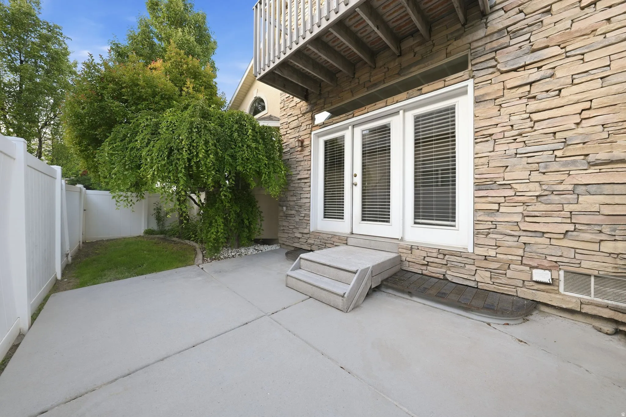 Private outdoor patio area featuring a stone veneer exterior, double French doors with integrated blinds, and a white vinyl privacy fence
