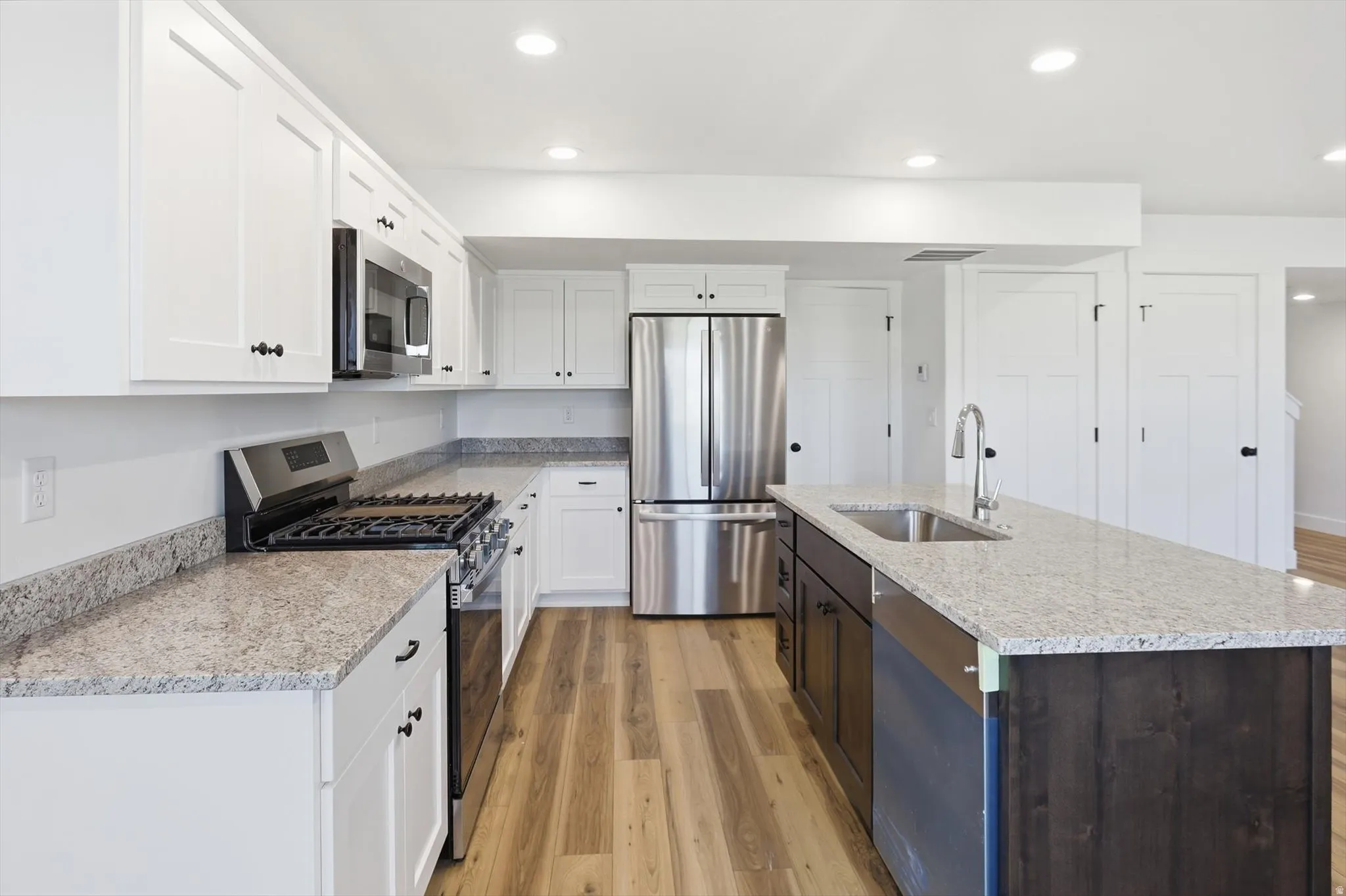 Kitchen featuring white cabinetry, stainless steel appliances, a center island with sink, ample counter space, and wood-finish flooring